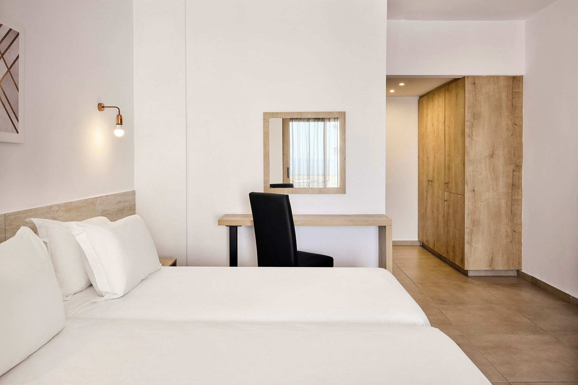 Valoisa hotellihuone, jossa on sänky, kirjoituspöytä, tuoli ja vaatekaappi. (Tekoälyn luoma teksti)