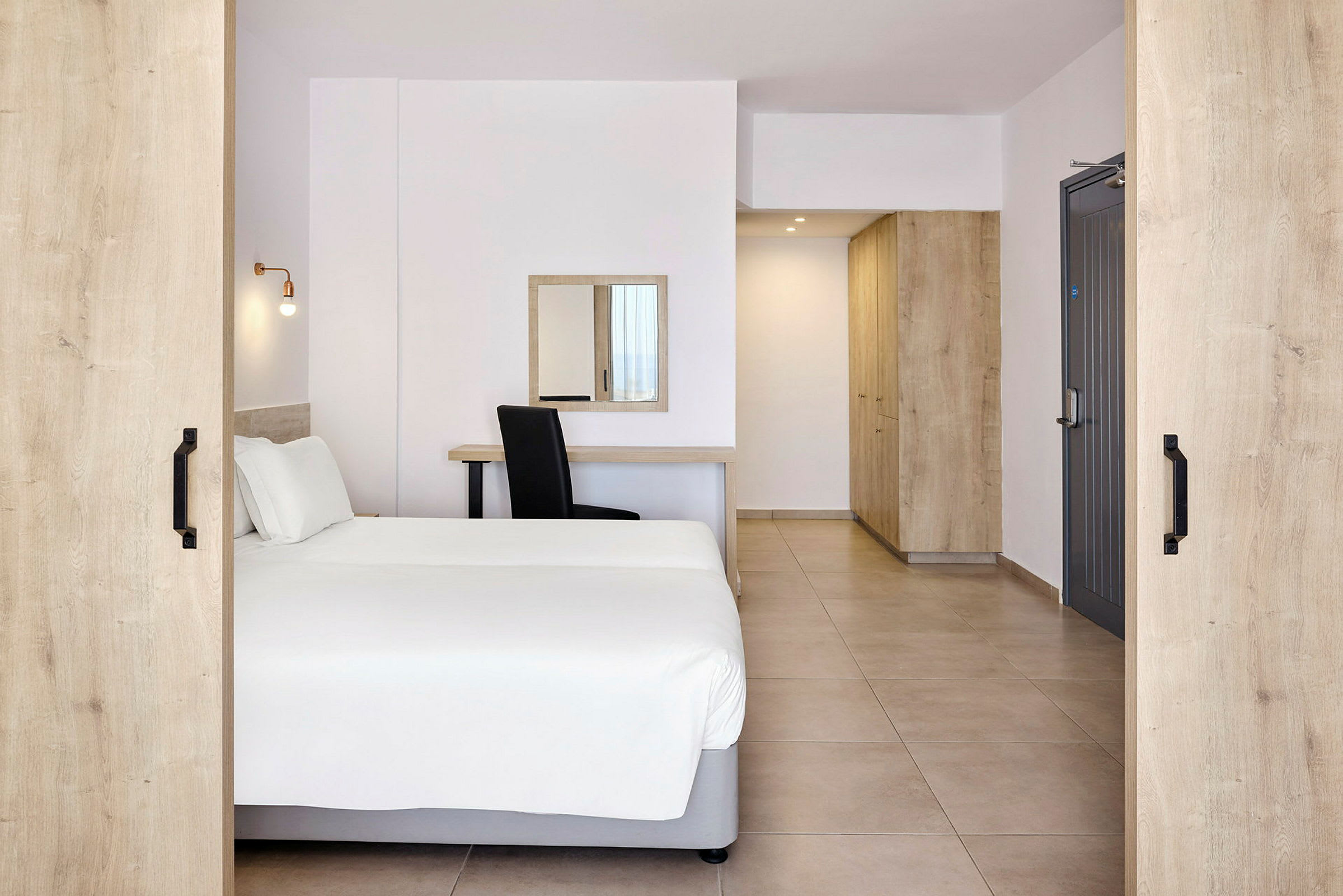Hotellihuone, jossa on parivuode, kirjoituspöytä, peili ja säilytyskalusteet. (Tekoälyn luoma teksti)