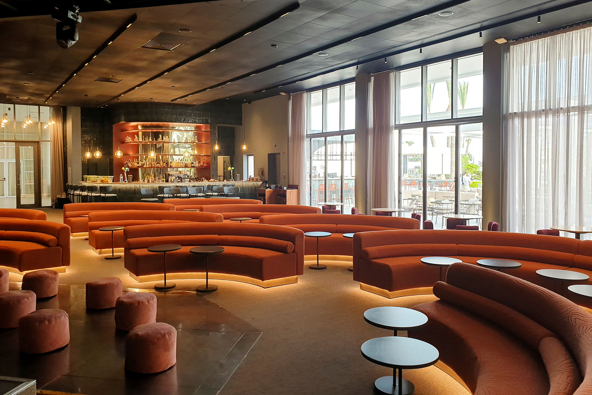 Moderni lounge, jossa on oransseja sohvia, pyöreitä pieniä pöytiä ja taustalla baari. (Tekoälyn luoma teksti)