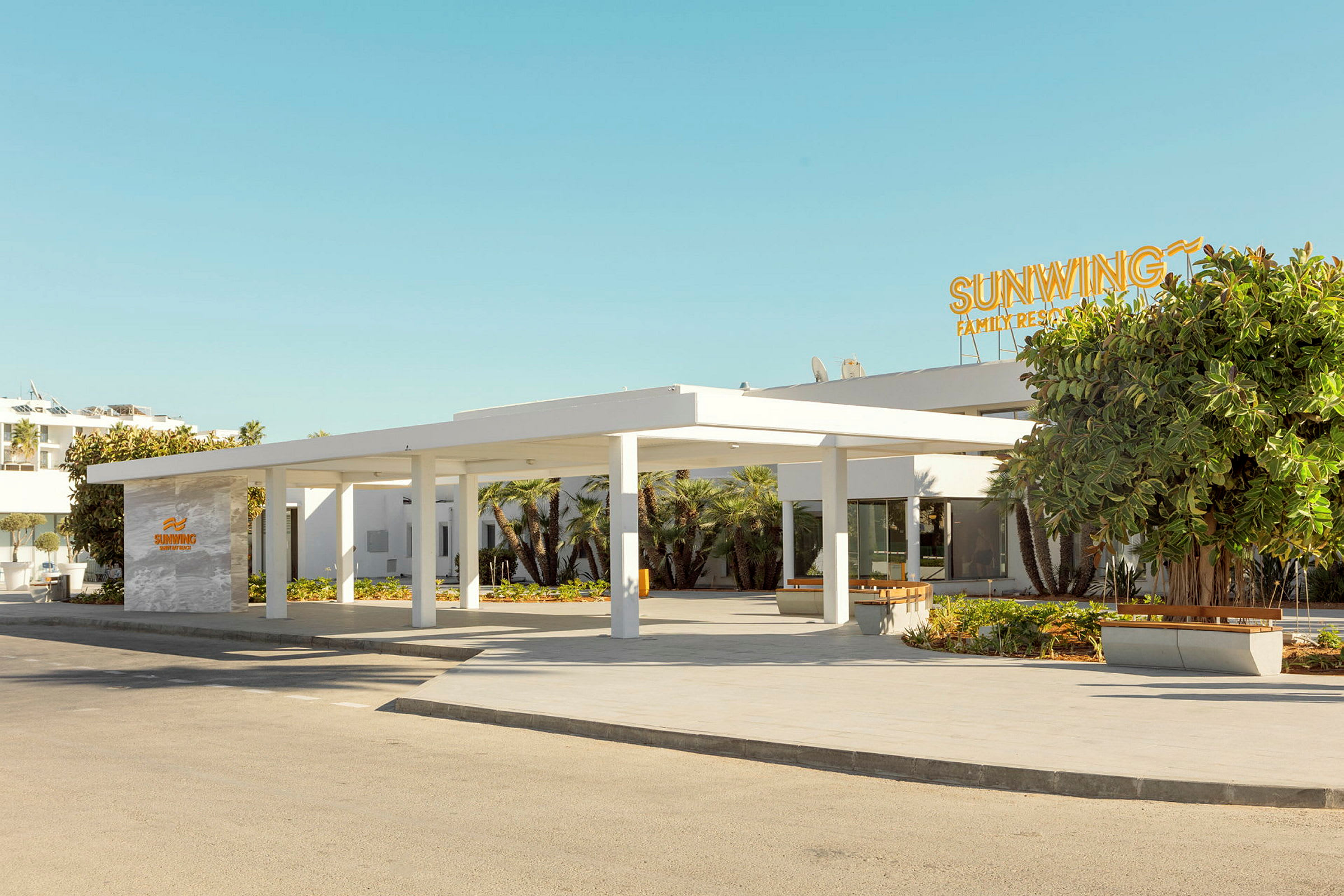 Kuva nykyaikaisen hotellin sisäänkäynnistä, jossa on valkoinen julkisivu ja kyltti, jossa lukee Sunwing Family Resort. (Tekoälyn luoma teksti)