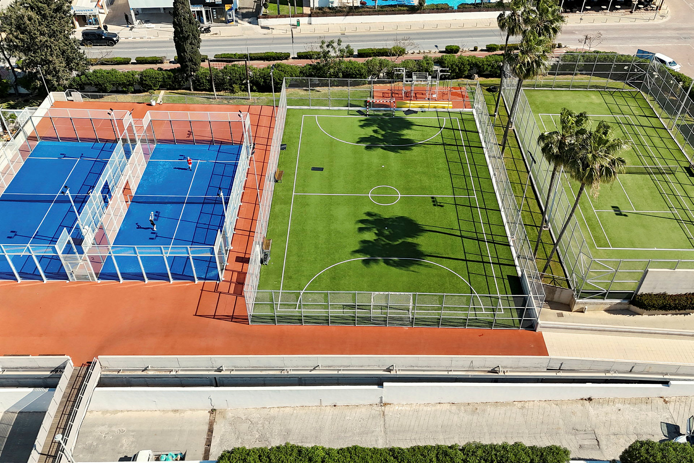 Kuva useista kentistä ulkona, mukaan lukien sininen tennis- tai padelkenttä ja vihreä jalkapallokenttä. (Tekoälyn luoma teksti)