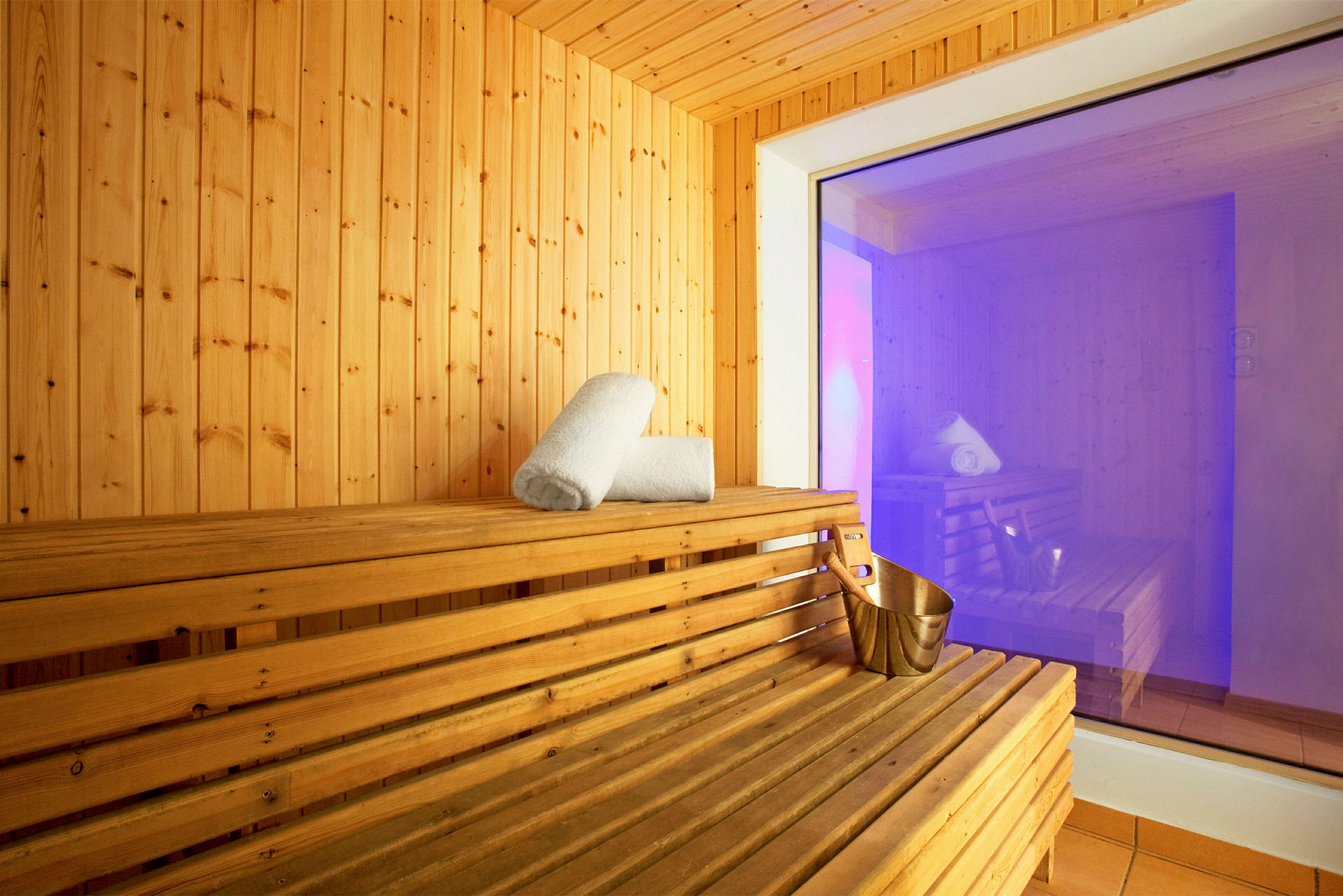 Sauna puuseinillä ja -penkeillä. Penkillä on rullalla oleva pyyhe ja metallikauha. (Tekoälyn luoma teksti)