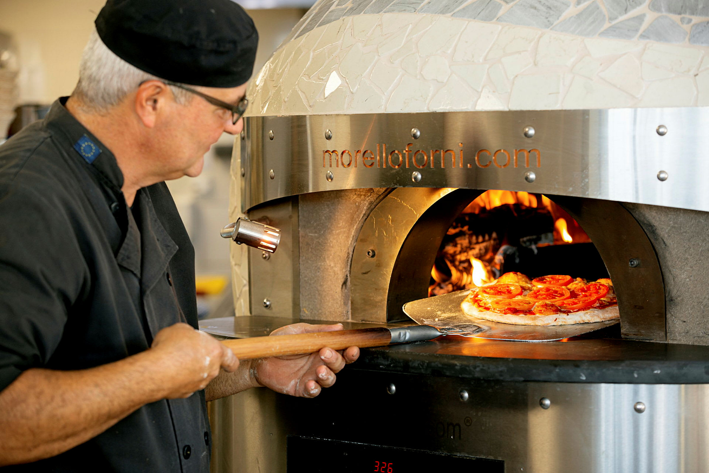 Pizzaa asetetaan puulämmitteiseen uuniin pizzalastalla. (Tekoälyn luoma teksti)