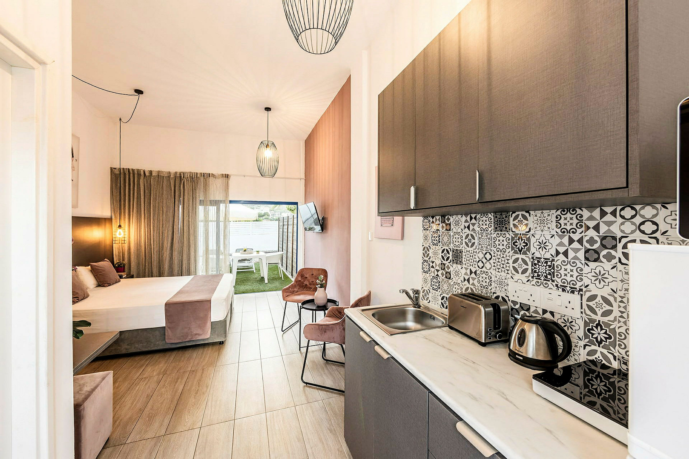 Kuvassa hotellihuone, jossa on keittiö ja makuutila, vaaleat kalusteet ja tyylikäs sisustus. (Tekoälyn luoma teksti)