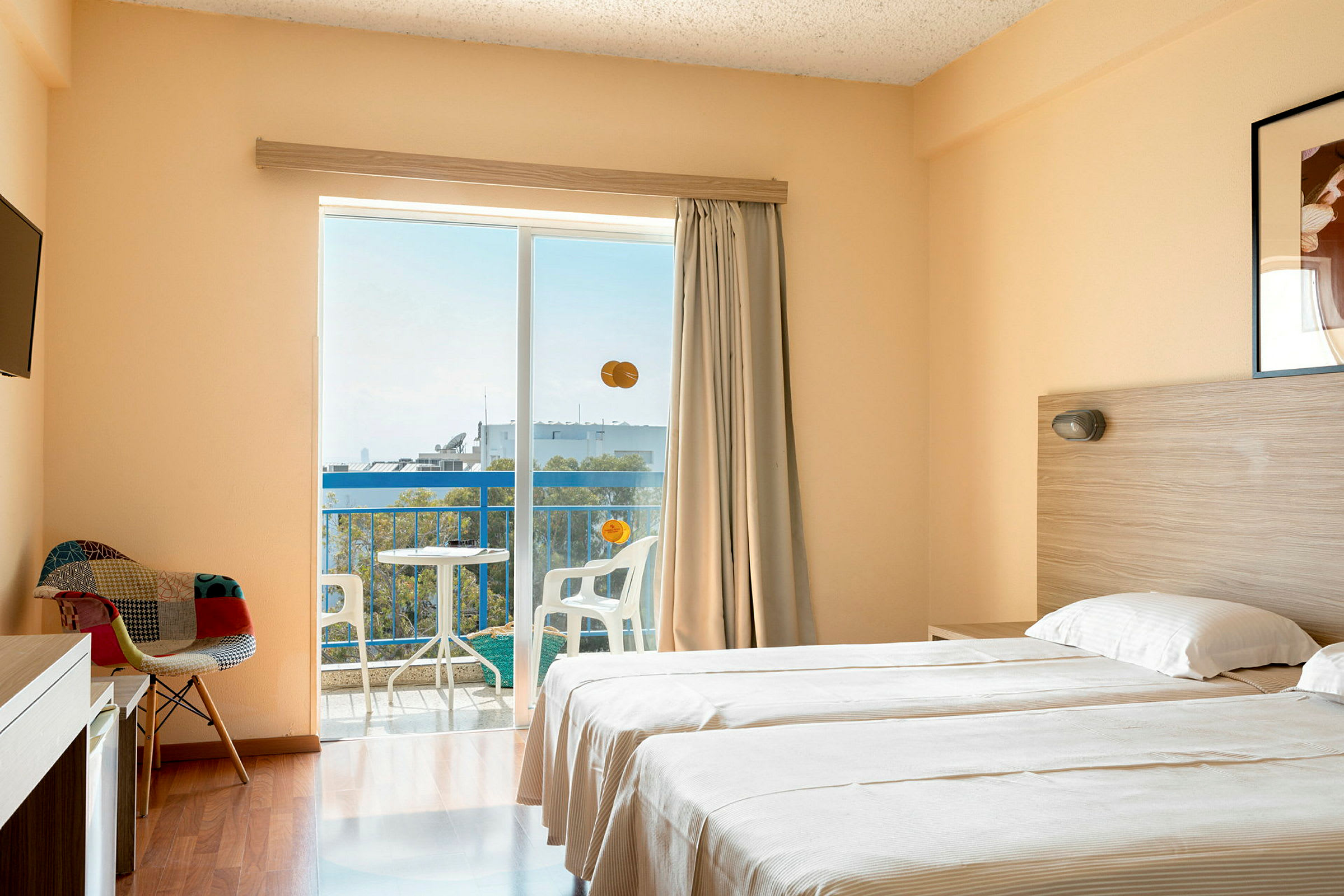 Hotellihuone, jossa on kaksi yhden hengen vuodetta, tuoli, televisio ja parveke, josta on näkymä. (Tekoälyn luoma teksti)