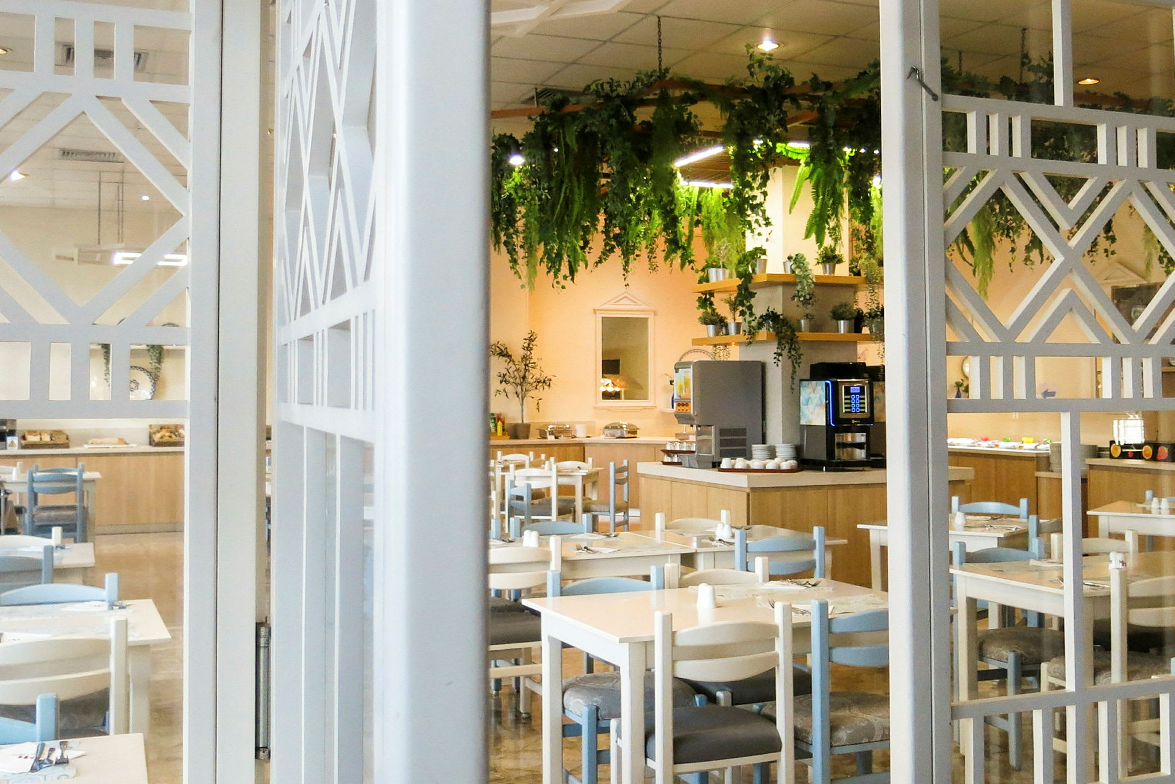 Ravintola, jossa on pöytiä ja tuoleja, sekä koristeltu buffet ja roikkuvia kasveja. (Tekoälyn luoma teksti)