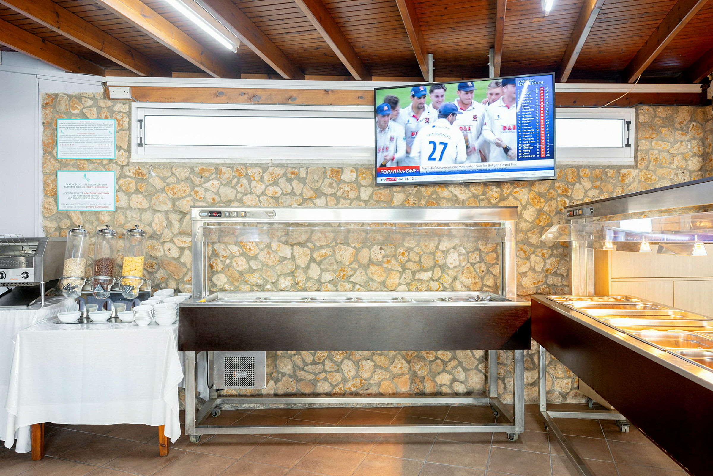 Buffet-alue, jossa tarjoilupisteitä ja seinälle kiinnitetty televisio. (Tekoälyn luoma teksti)