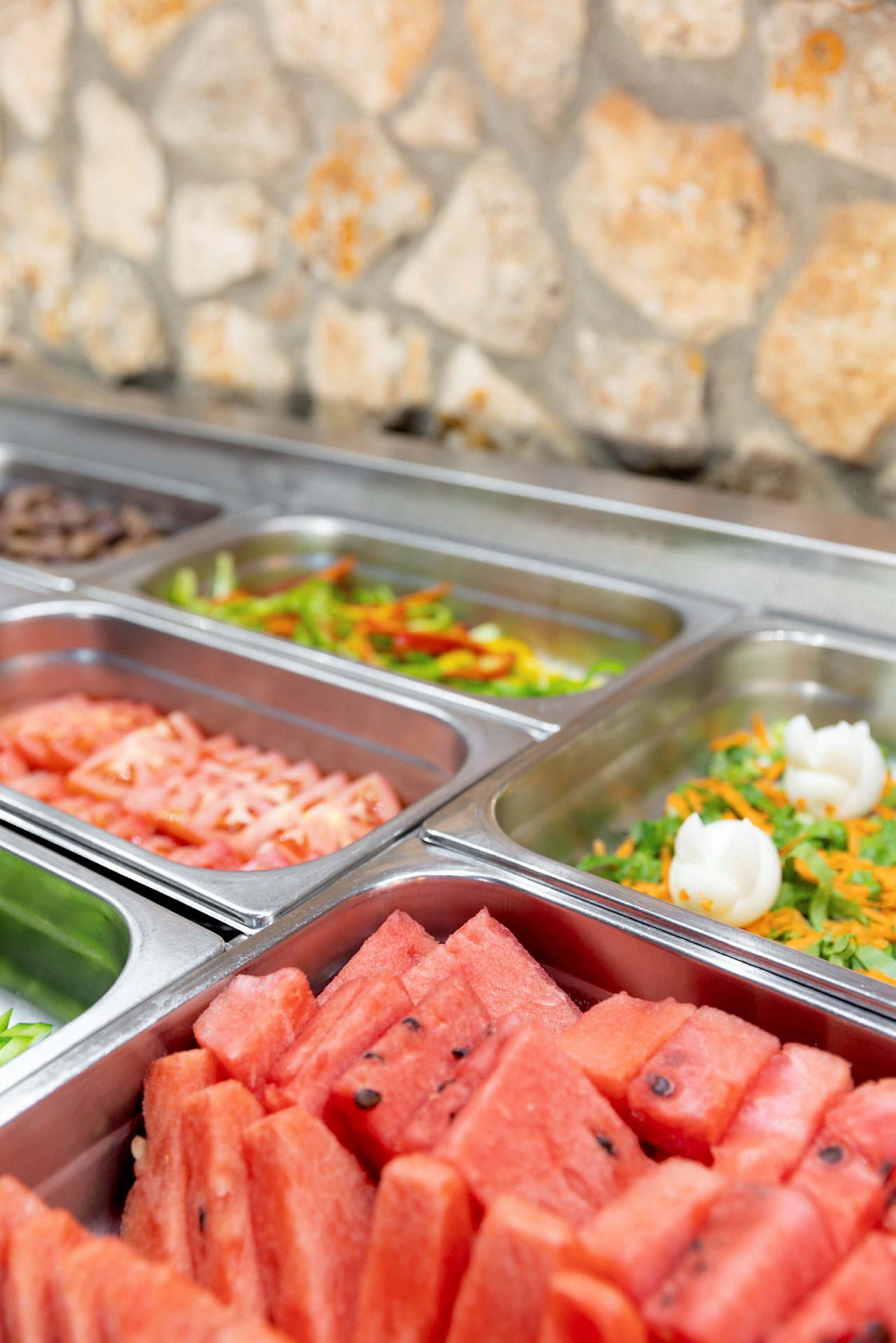Buffetin lähikuva, jossa erilaisia ruokavaihtoehtoja tarjoiluastioissa. (Tekoälyn luoma teksti)