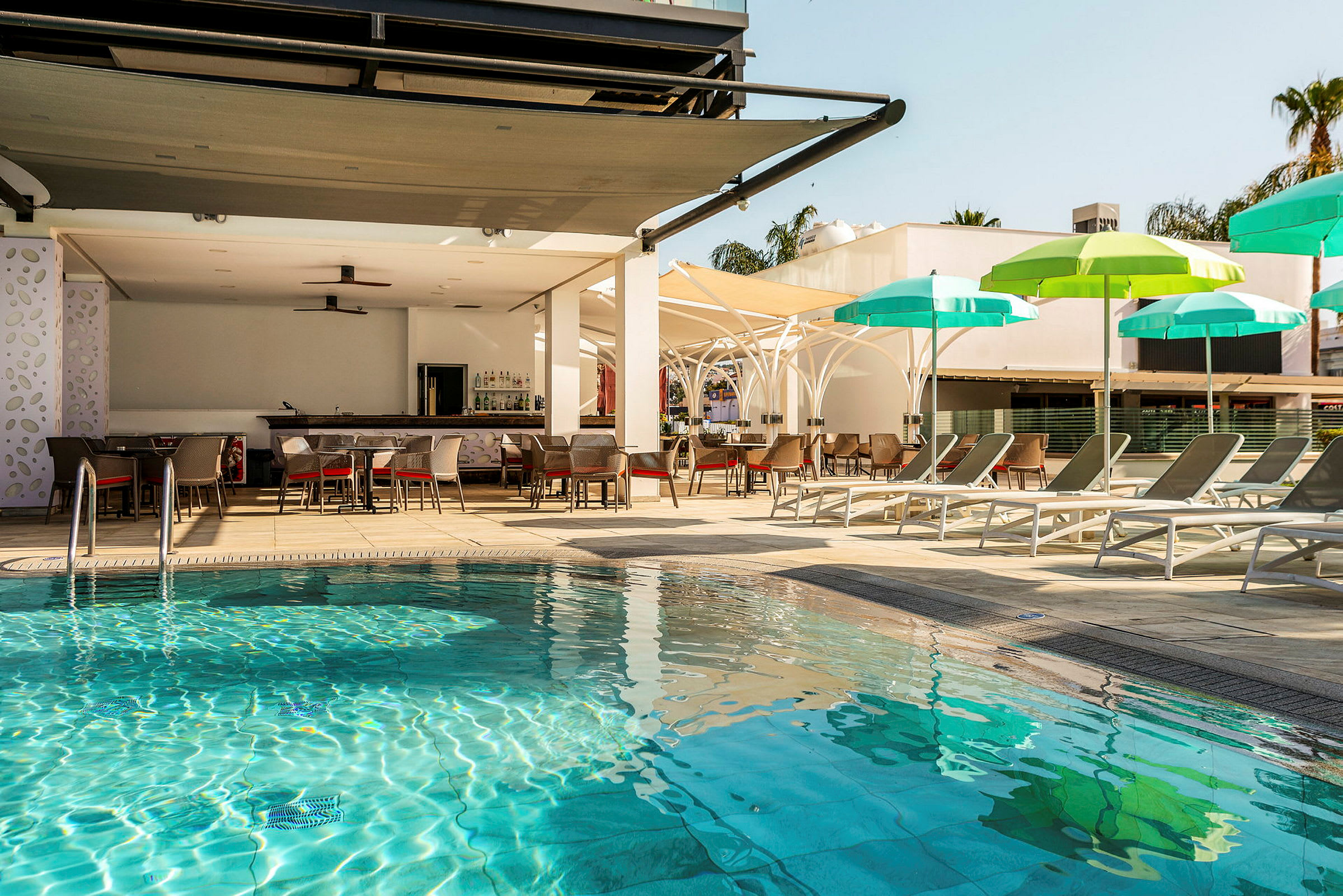 Uima-allasalue, jossa aurinkotuoleja ja varjoja sekä baari taustalla. (Tekoälyn luoma teksti)