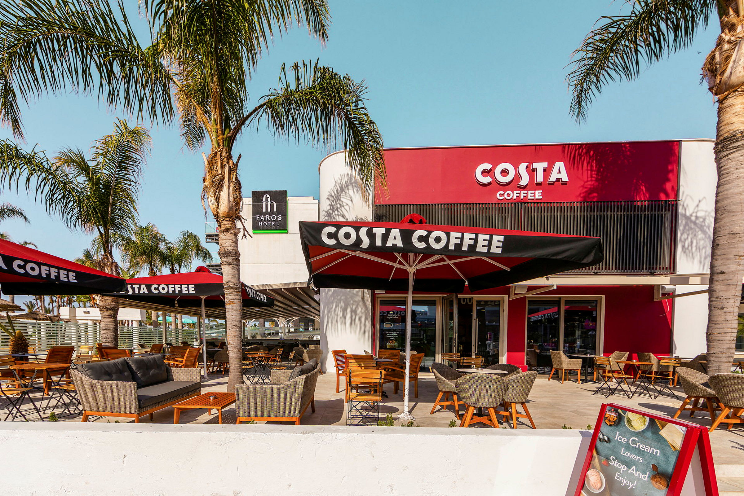 Kahvila Costa Coffeen ulkoterassi, jossa palmuja ja istumapaikkoja. (Tekoälyn luoma teksti)