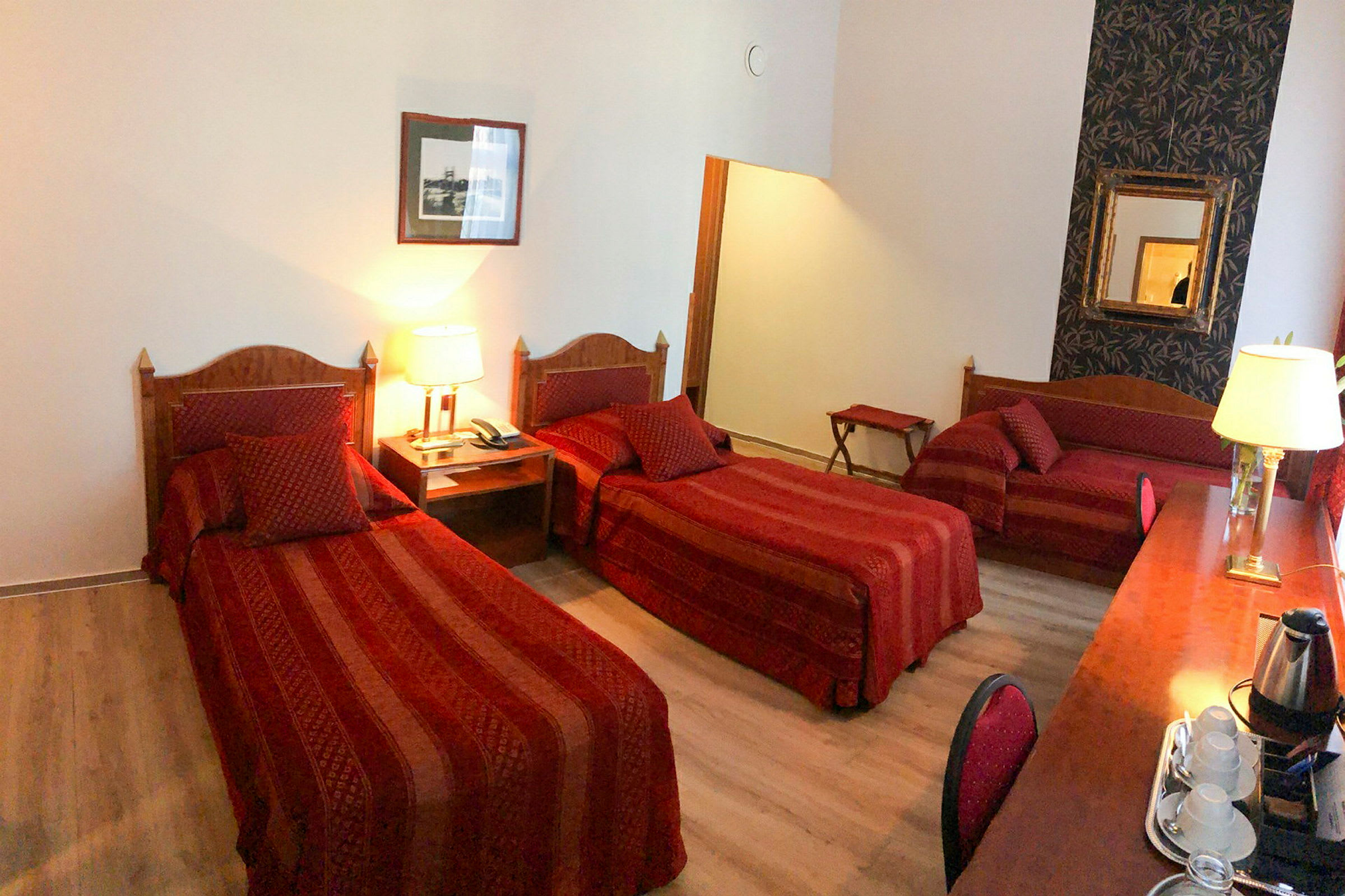 Hotellihuone, jossa on kolme vuodetta tilavassa tilassa, sisustettu punaisilla tekstiileillä ja puukoristeilla. (Tekoälyn luoma teksti)