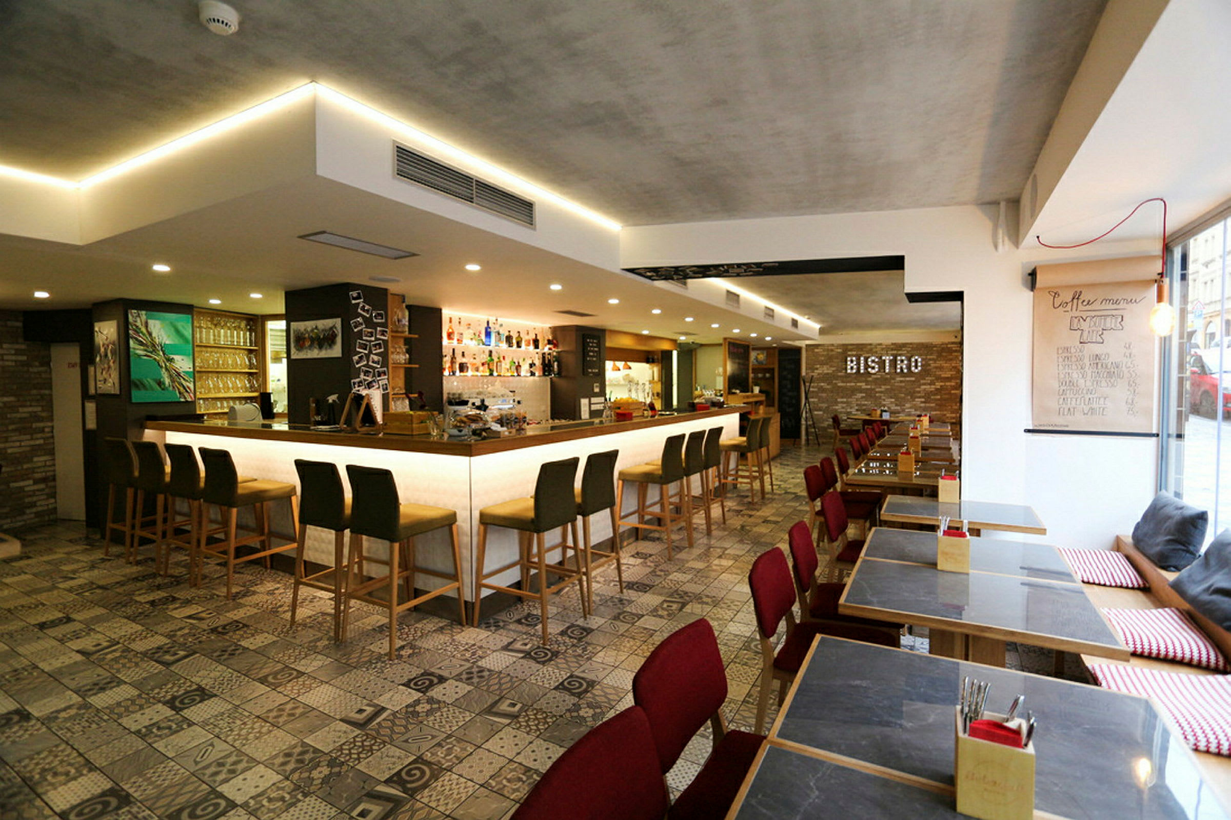 Modernin bistrotarjoilun sisustus, jossa baarituolit valaistun baaritiskin edessä ja ruokapöytiä punaisilla tuoleilla. (Tekoälyn luoma teksti)