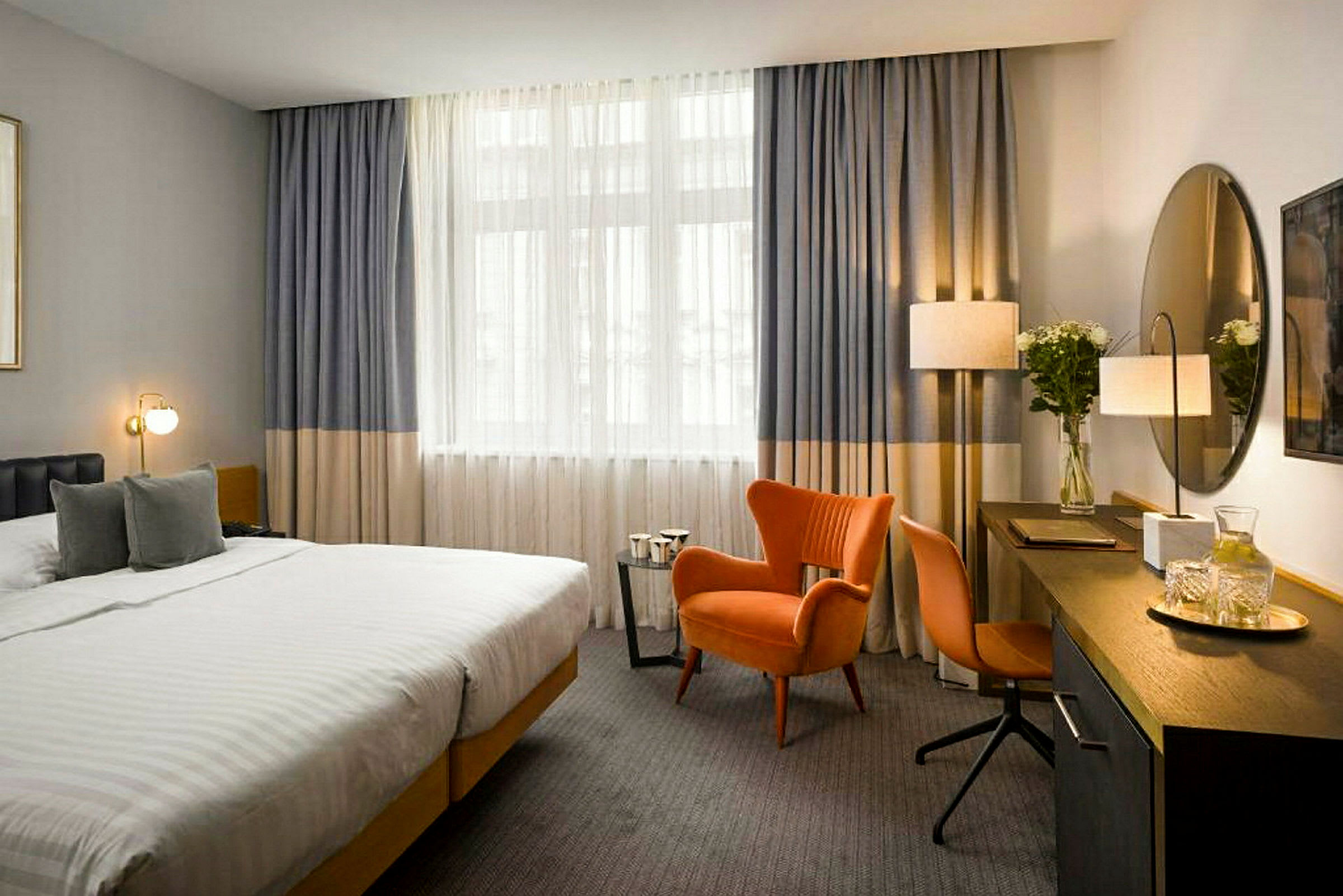 Hotellihuone, jossa iso sänky, oranssi nojatuoli ja työpöytä peilillä. (Tekoälyn luoma teksti)