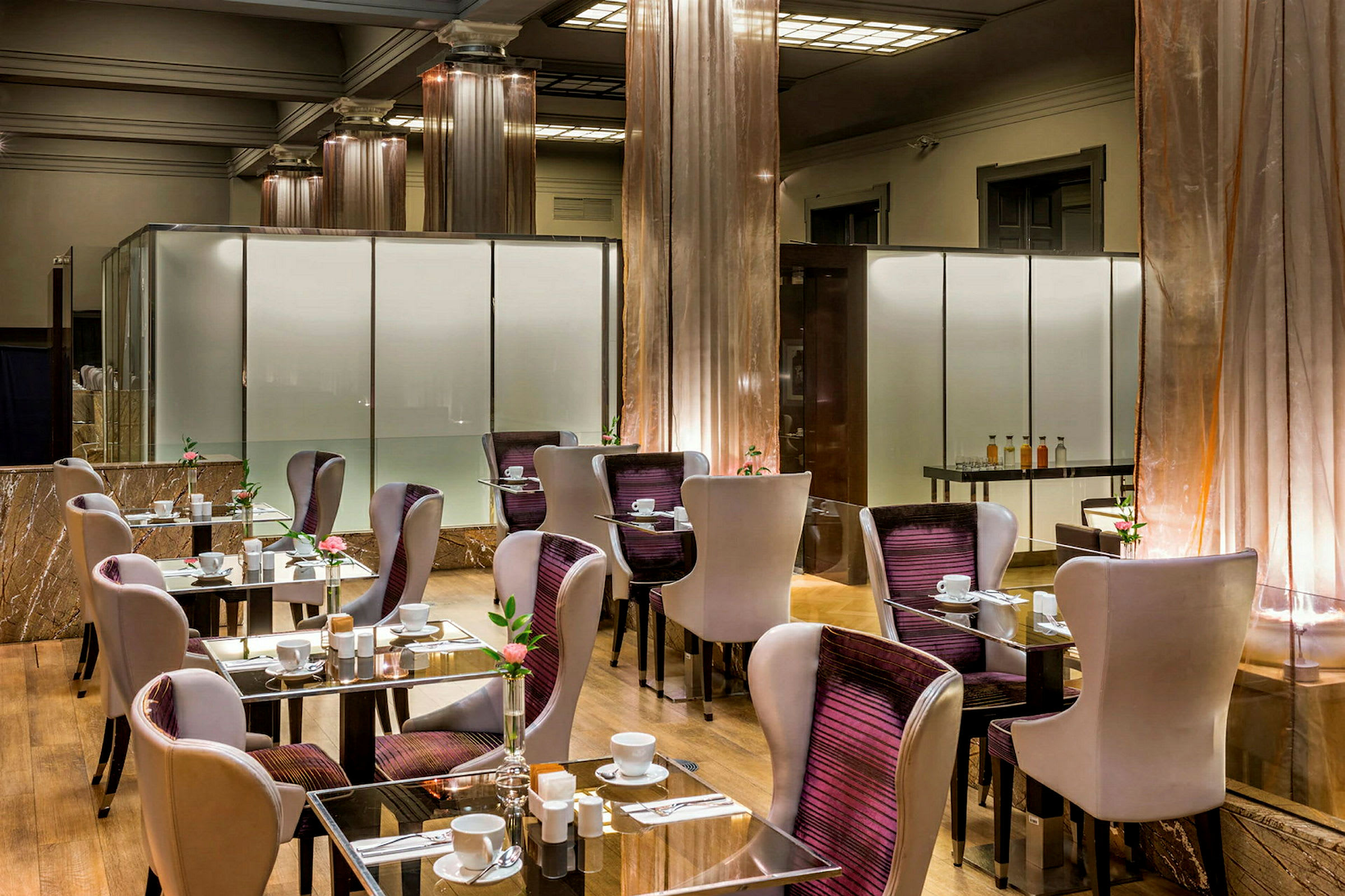 Moderni ravintola pöytineen ja tuoleineen. Lasi pöydät kattauksin ja kukkakoristein. (Tekoälyn luoma teksti)