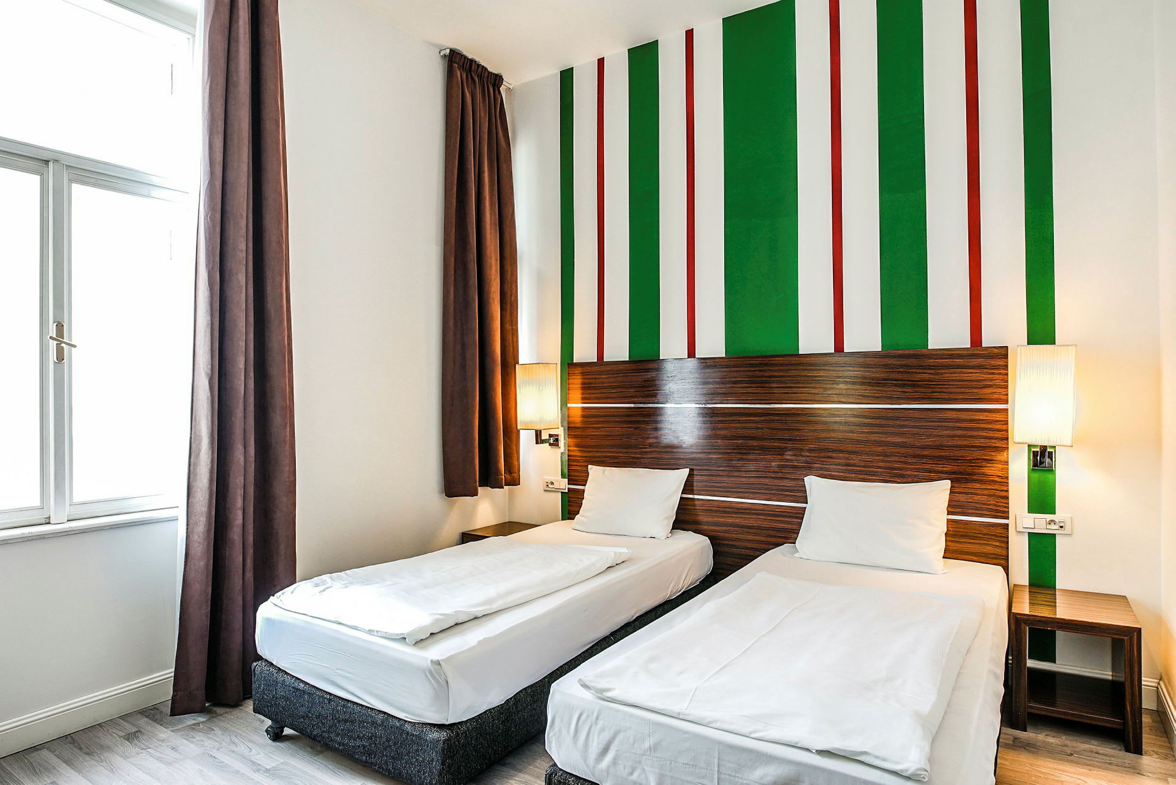 Hotellihuone, jossa kaksi yhden hengen vuodetta, moderni sisustus vaaleilla väreillä ja raidallinen seinäkoriste. (Tekoälyn luoma teksti)