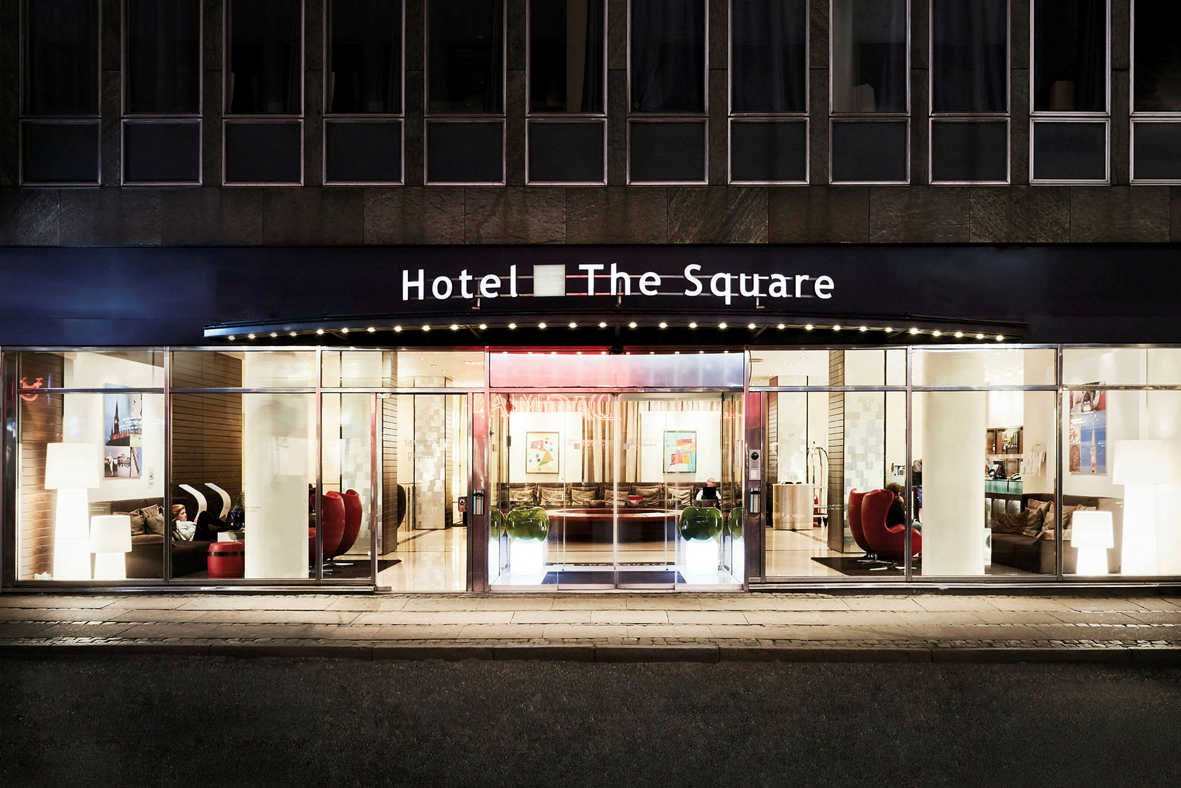 Hotellin sisäänkäynti nimeltä "The Square" valaistuna illalla. (Tekoälyn luoma teksti)
