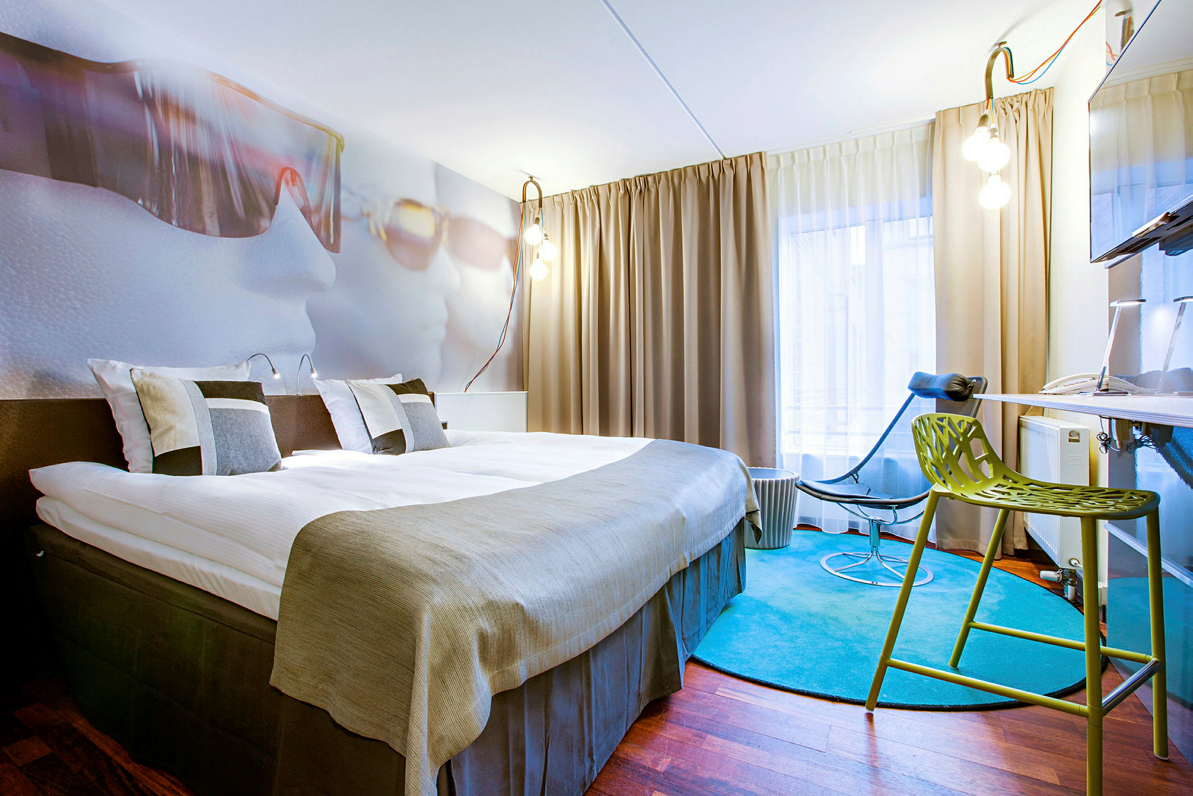 Hotellihuone, jossa on iso sänky, nykyaikaiset huonekalut ja värikäs matto. (Tekoälyn luoma teksti)