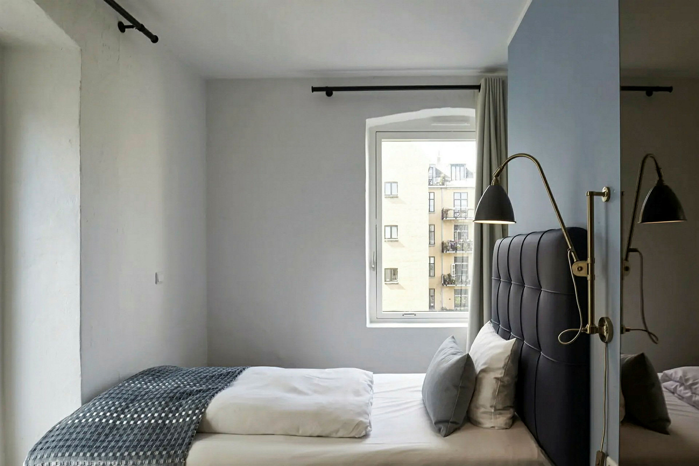 Hotellihuone, jossa on sänky lähellä ikkunaa ja seinälamput kiinnitettyinä sängynpäätyyn. (Tekoälyn luoma teksti)