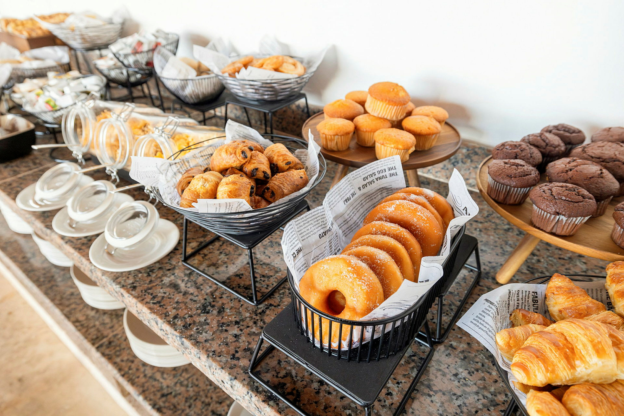 Buffet, jossa on erilaisia leivonnaisia, kuten muffineita, kroissantteja ja munkkeja. (Tekoälyn luoma teksti)