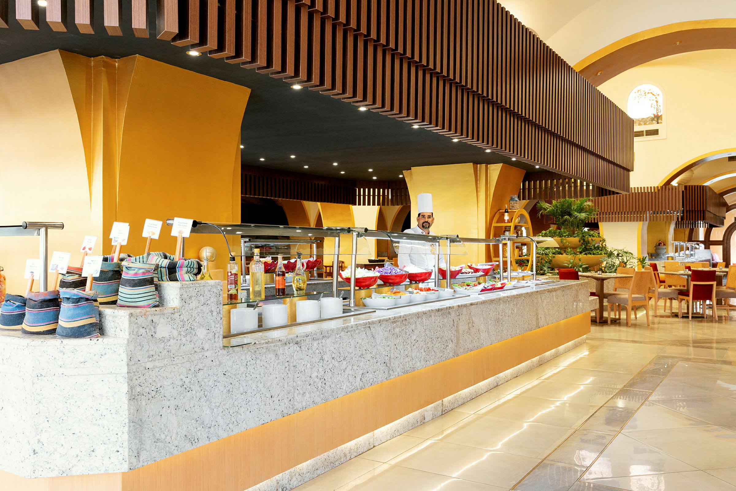 Buffet-ravintola, jossa on keltaiset sisustuselementit ja vaaleat tasot. (Tekoälyn luoma teksti)
