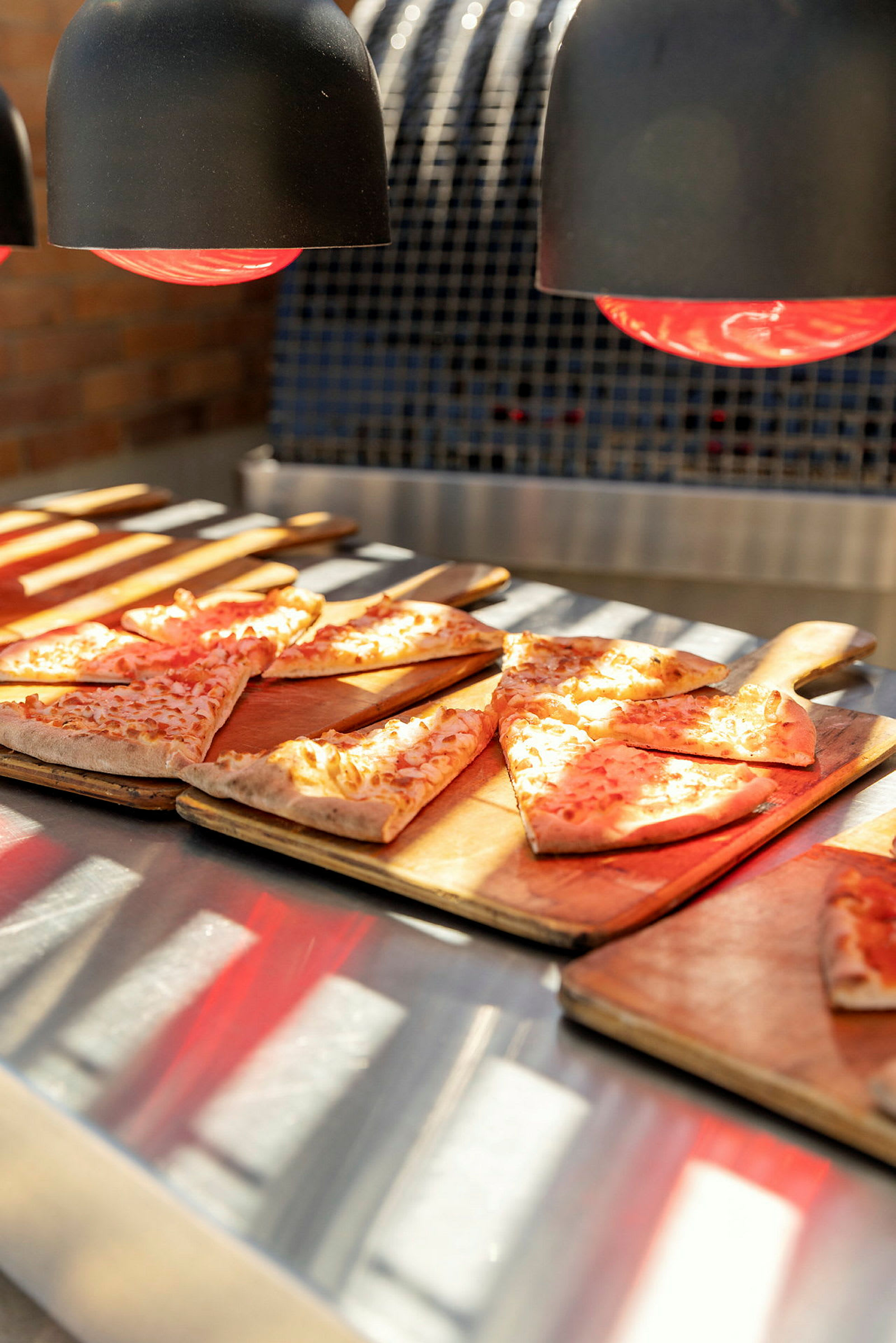 Pizzaa leikkuulaudoilla lämpölampun alla. (Tekoälyn luoma teksti)