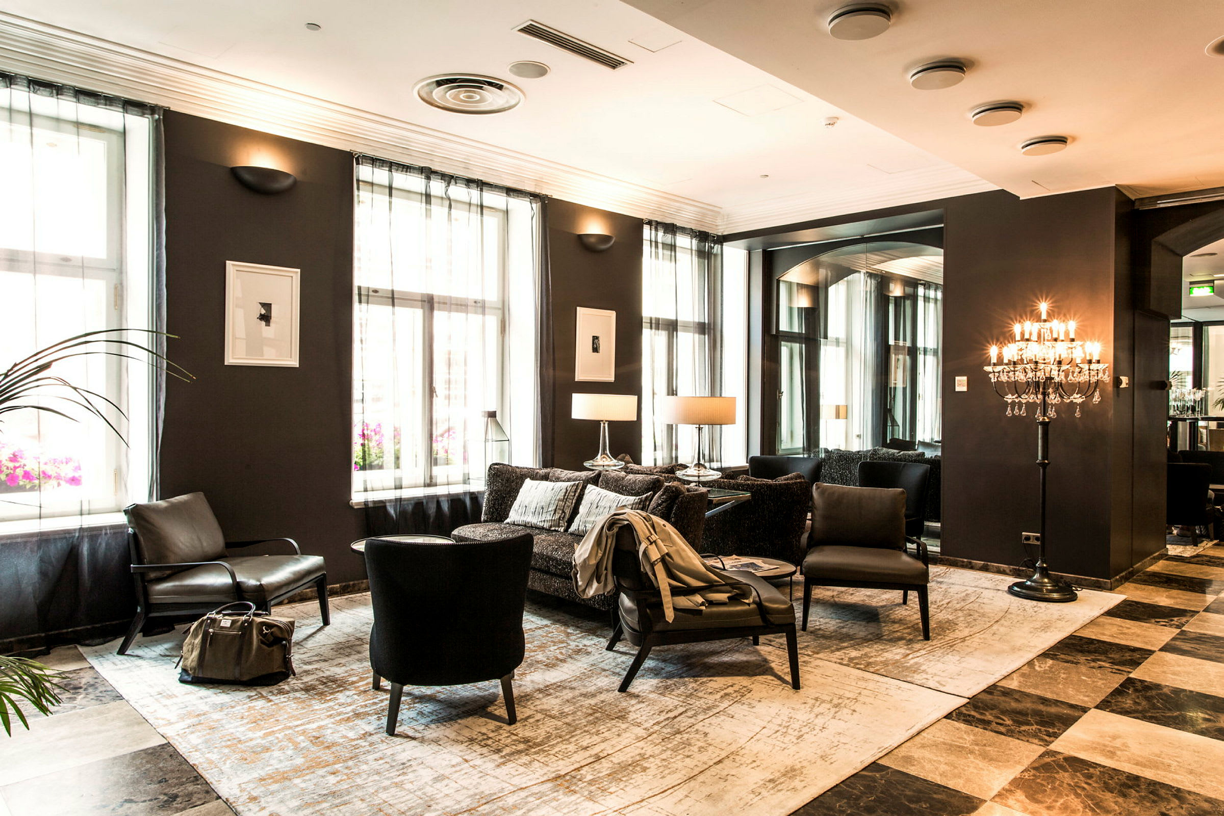 Eleganttinen hotellihuone, jossa istuimia, seinävalaisimia ja ikkunoita vaaleilla verhoilla. (Tekoälyn luoma teksti)