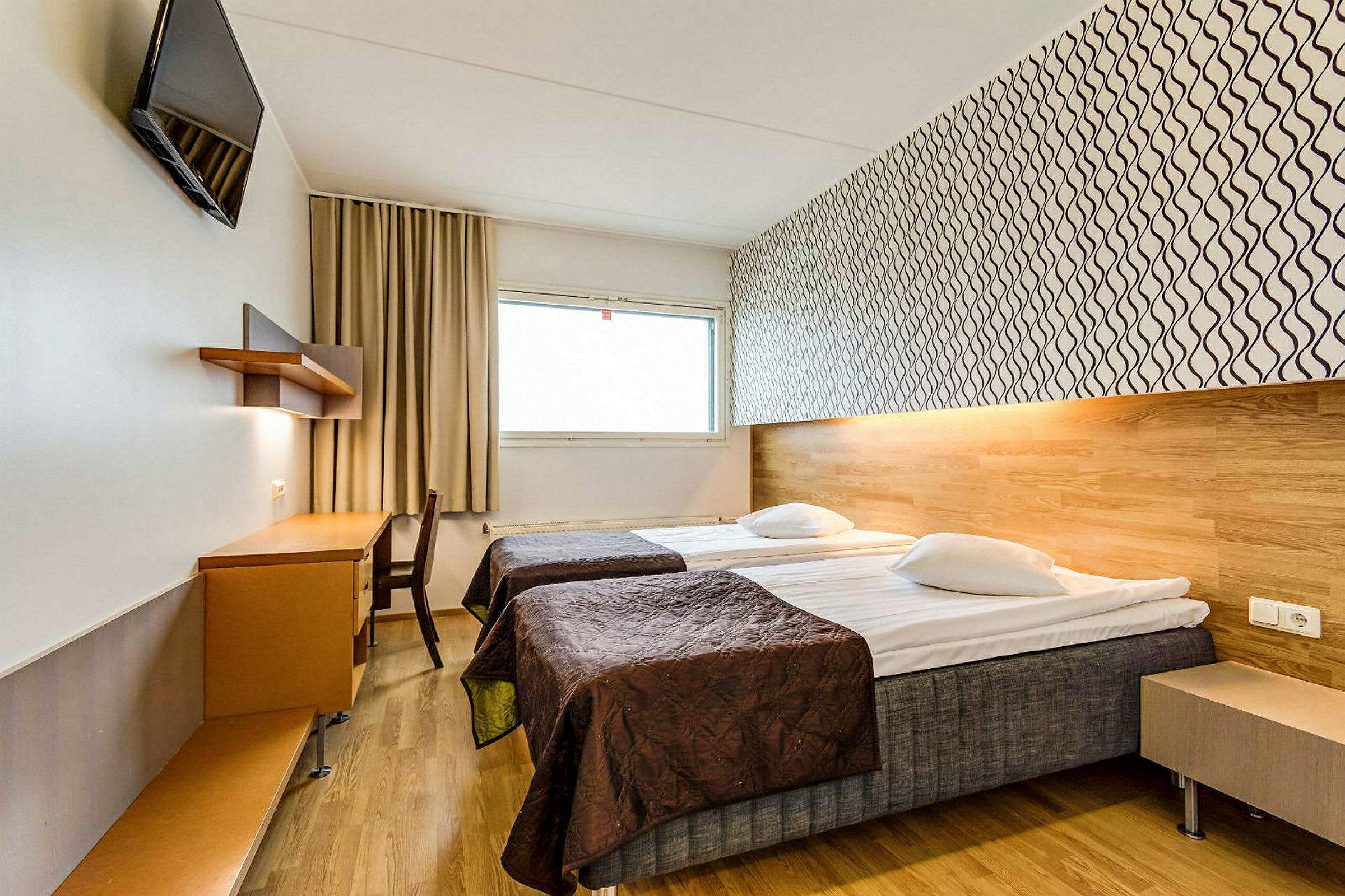 Hotellihuone, jossa on kaksi erillistä vuodetta, työpöytä ja seinään kiinnitetty televisio. (Tekoälyn luoma teksti)
