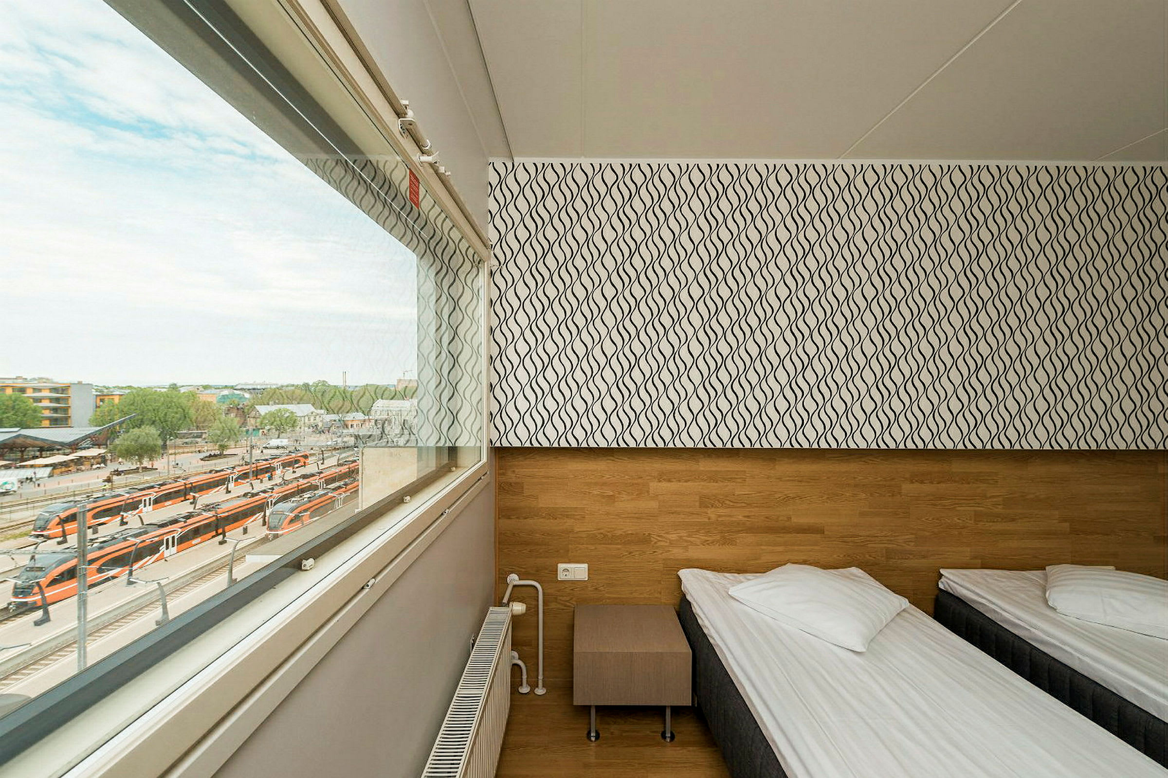 Yksinkertainen hotellihuone, jossa on kaksi erillistä vuodetta ja ikkuna, josta näkyy rautatieasema. (Tekoälyn luoma teksti)