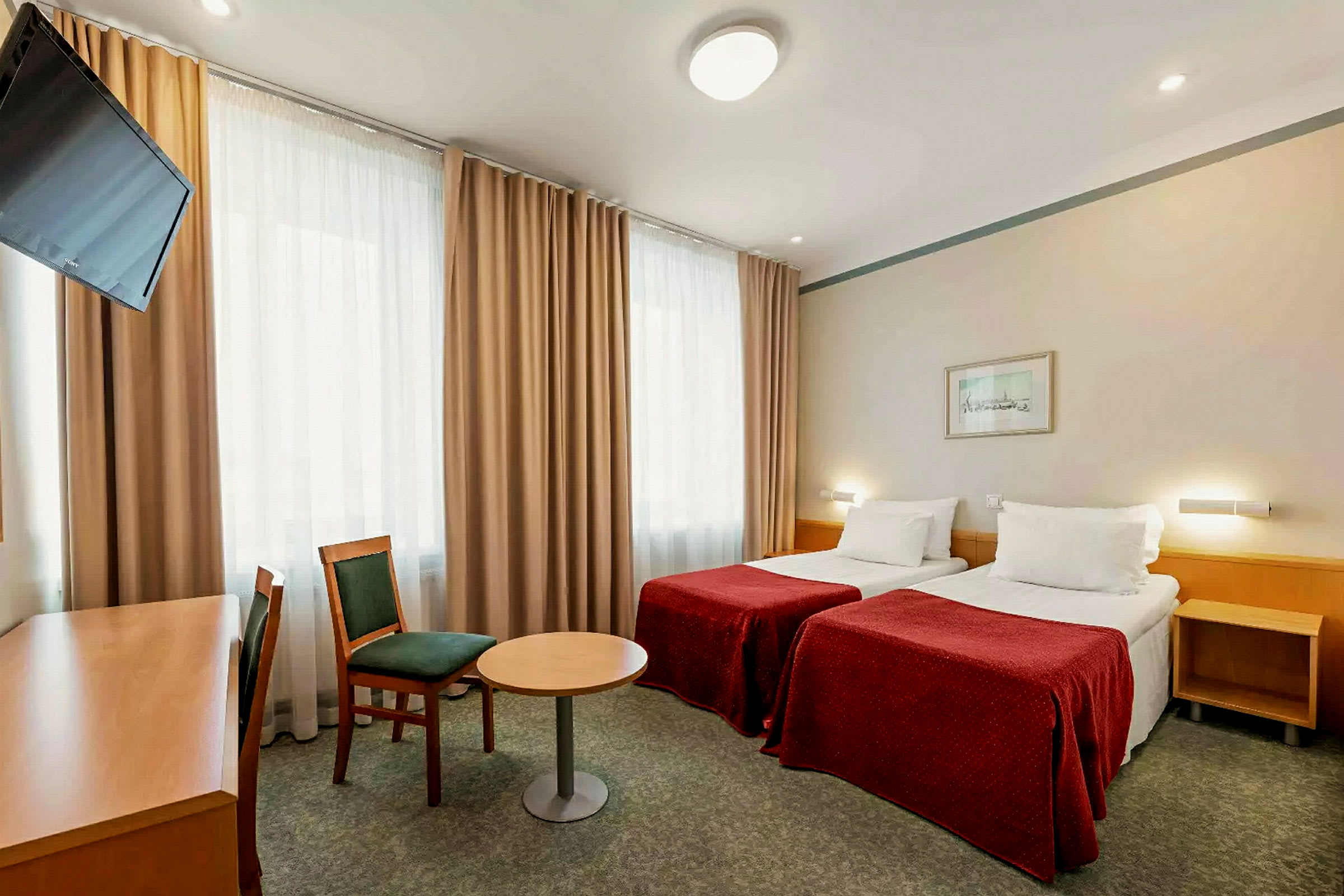 Hotellihuone, jossa kaksi erillistä vuodetta, tuoli, pöytä ja kirjoituspöytä, jonka edessä on televisio. (Tekoälyn luoma teksti)
