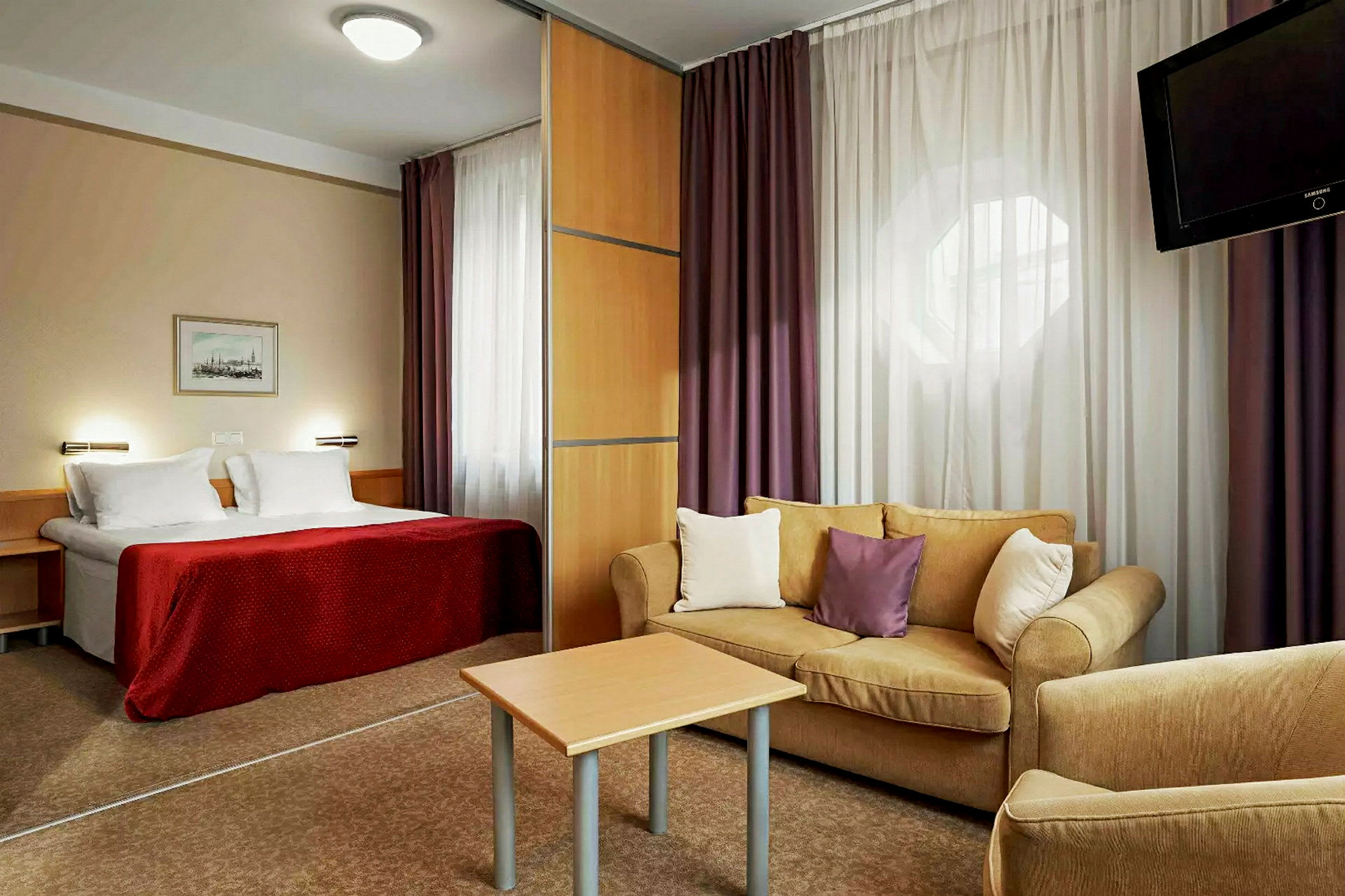 Hotellihuone, jossa sänky, olohuone sohvan ja pöydän kanssa sekä televisio. (Tekoälyn luoma teksti)