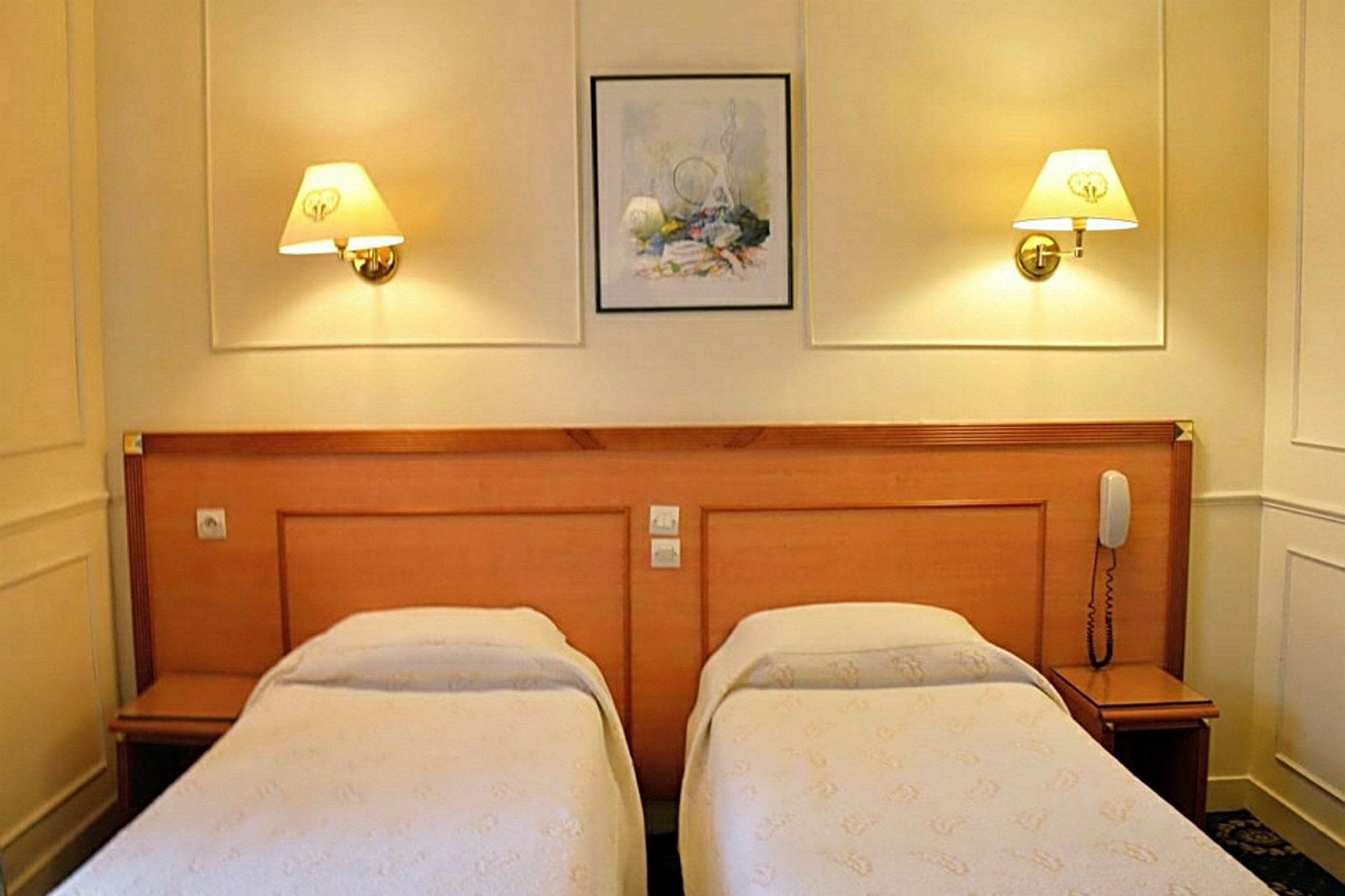 Hotellihuone, jossa on kaksi yhden hengen vuodetta ja seinävalaisimet. (Tekoälyn luoma teksti)