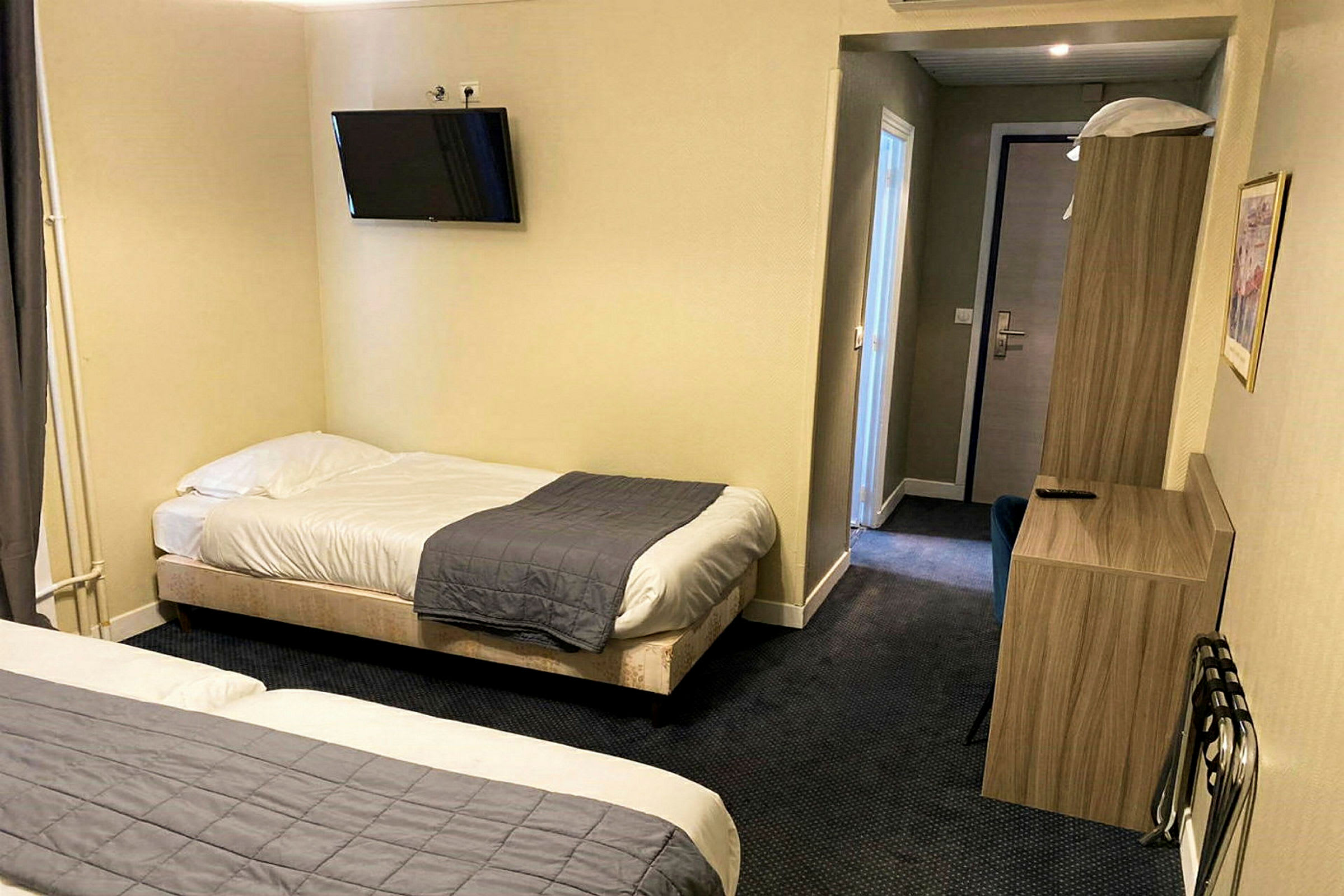 Hotellihuone, jossa on kaksi erillistä vuodetta, seinälle asennettu televisio ja huonekaluja. (Tekoälyn luoma teksti)