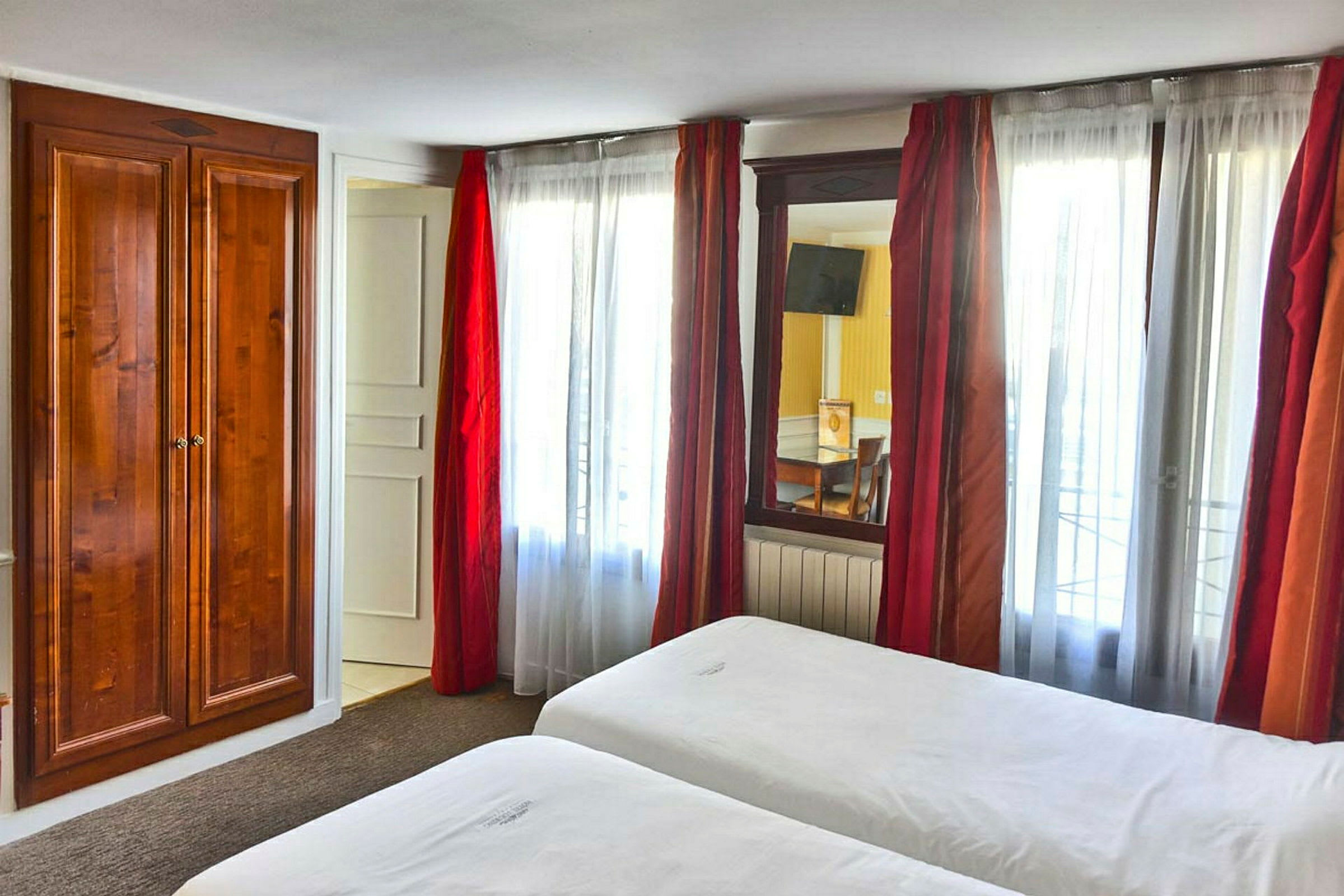 Hotellihuone, jossa on kaksi sänkyä, valkoiset lakanat ja puinen vaatekaappi ikkunan vieressä, jossa on punaiset verhot. (Tekoälyn luoma teksti)