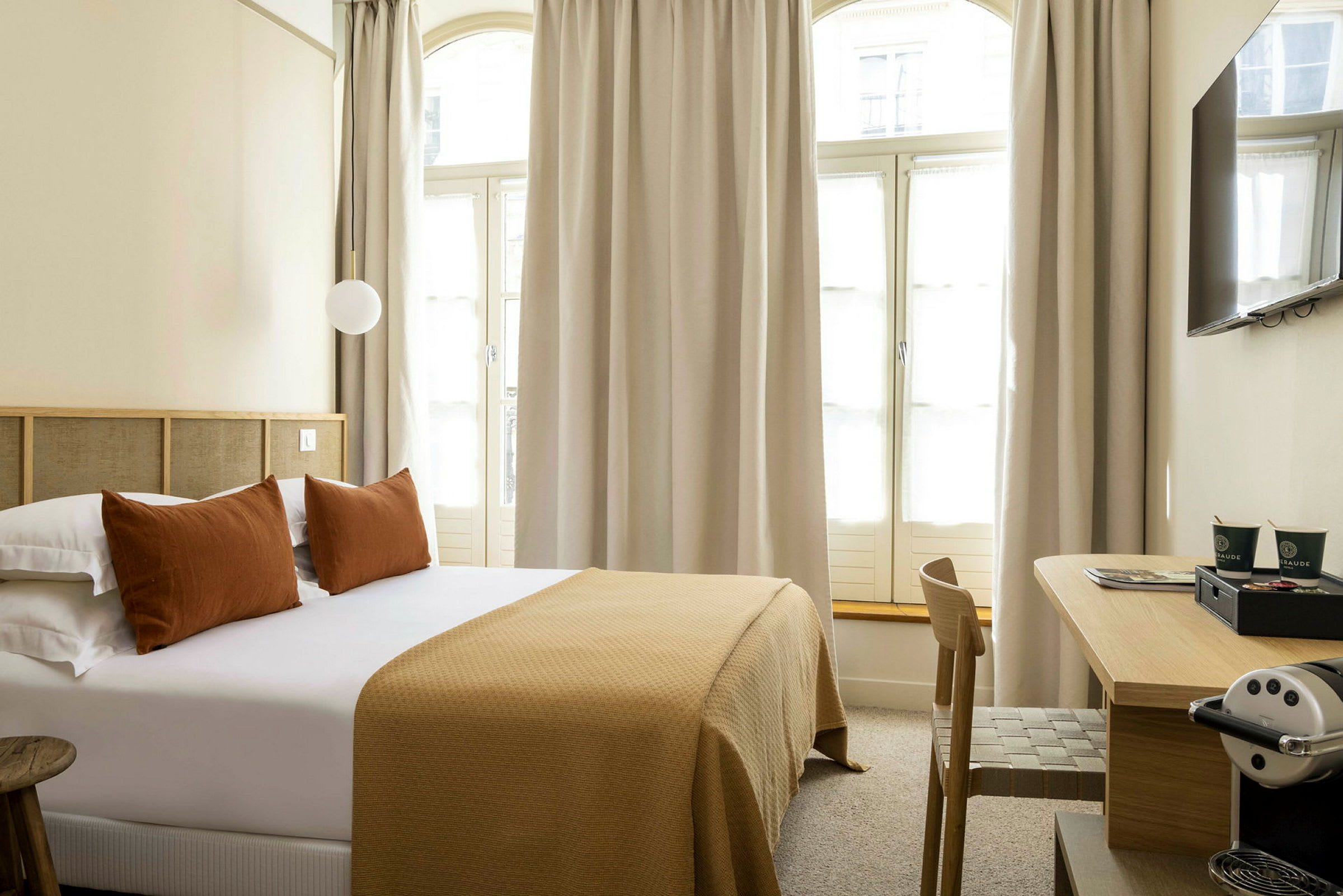 Hotellihuone, jossa on parivuode, tyynyt ja ruskeansävyinen peite sekä työpöytä ja kahvikone. (Tekoälyn luoma teksti)
