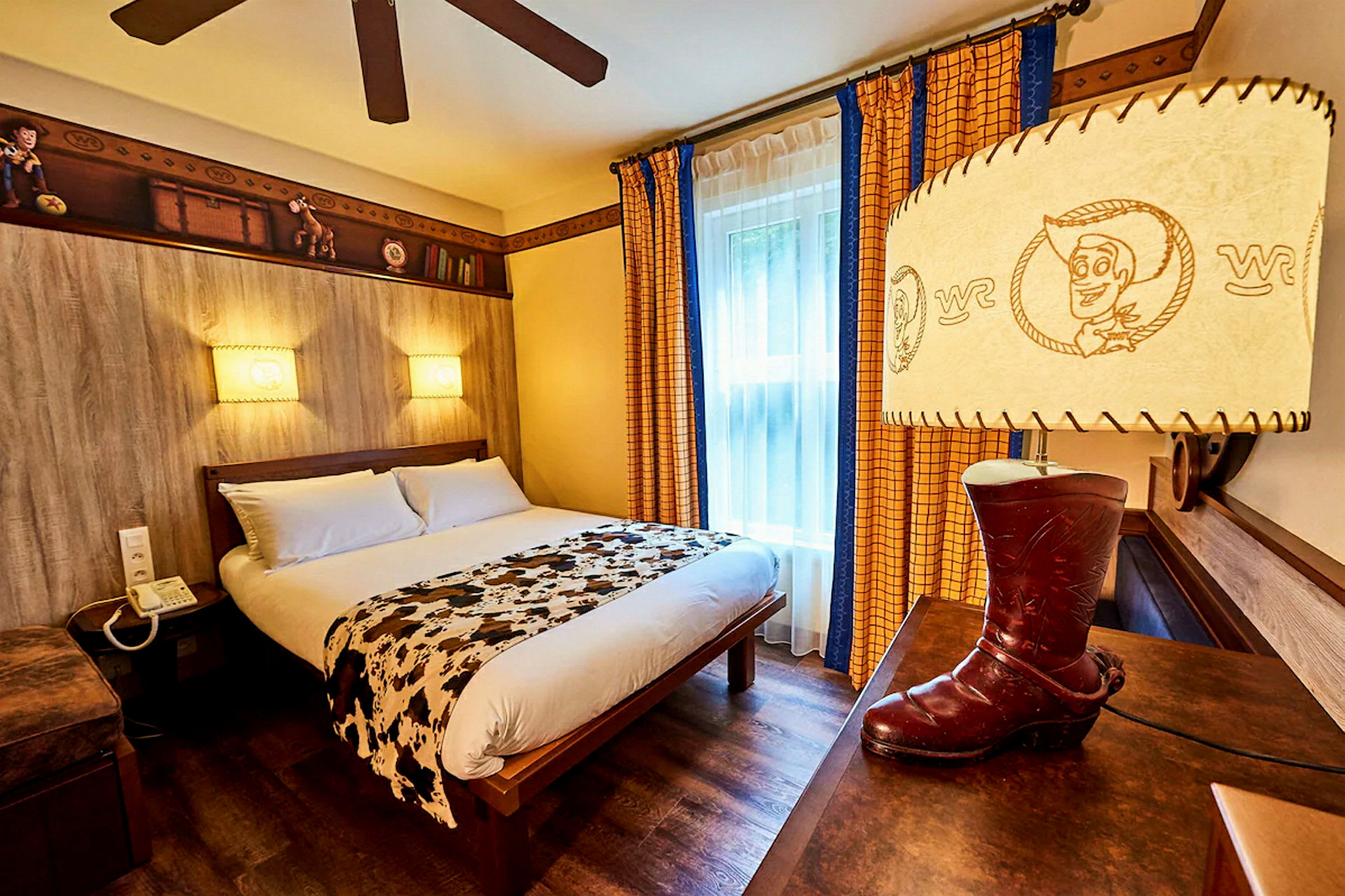 Teemallinen hotellihuone, jossa on parisänky, koristeltu leluinspiratuilla yksityiskohdilla ja cowboysaapasta muotoiltu lamppu. (Tekoälyn luoma teksti)