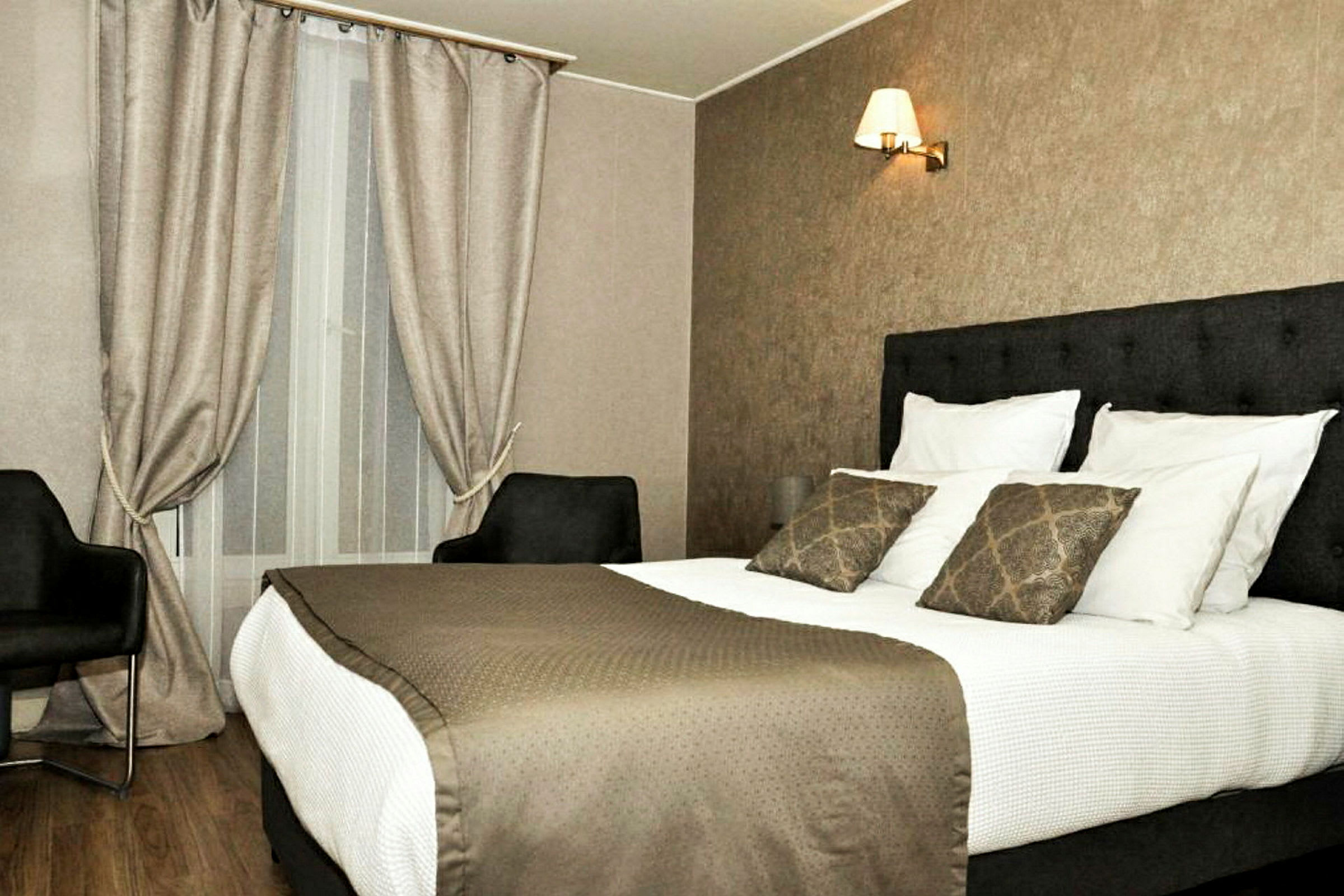 Hotellihuone, jossa on parivuode, kaksi nojatuolia ja ikkuna verhoilla. (Tekoälyn luoma teksti)