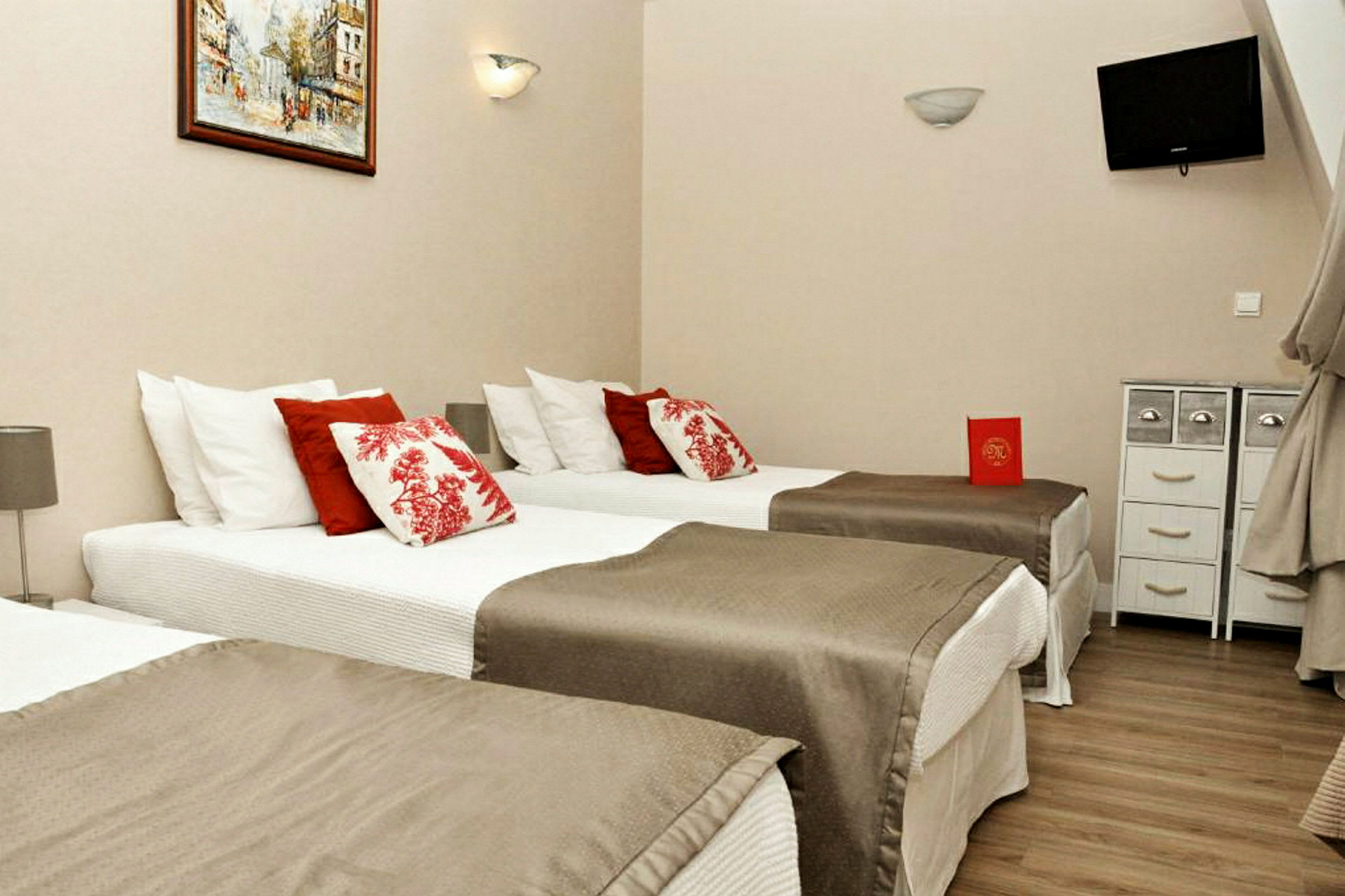 Hotellihuone, jossa on kolme yhden hengen vuodetta, koristeltu punaisilla ja valkoisilla tyynyillä. (Tekoälyn luoma teksti)