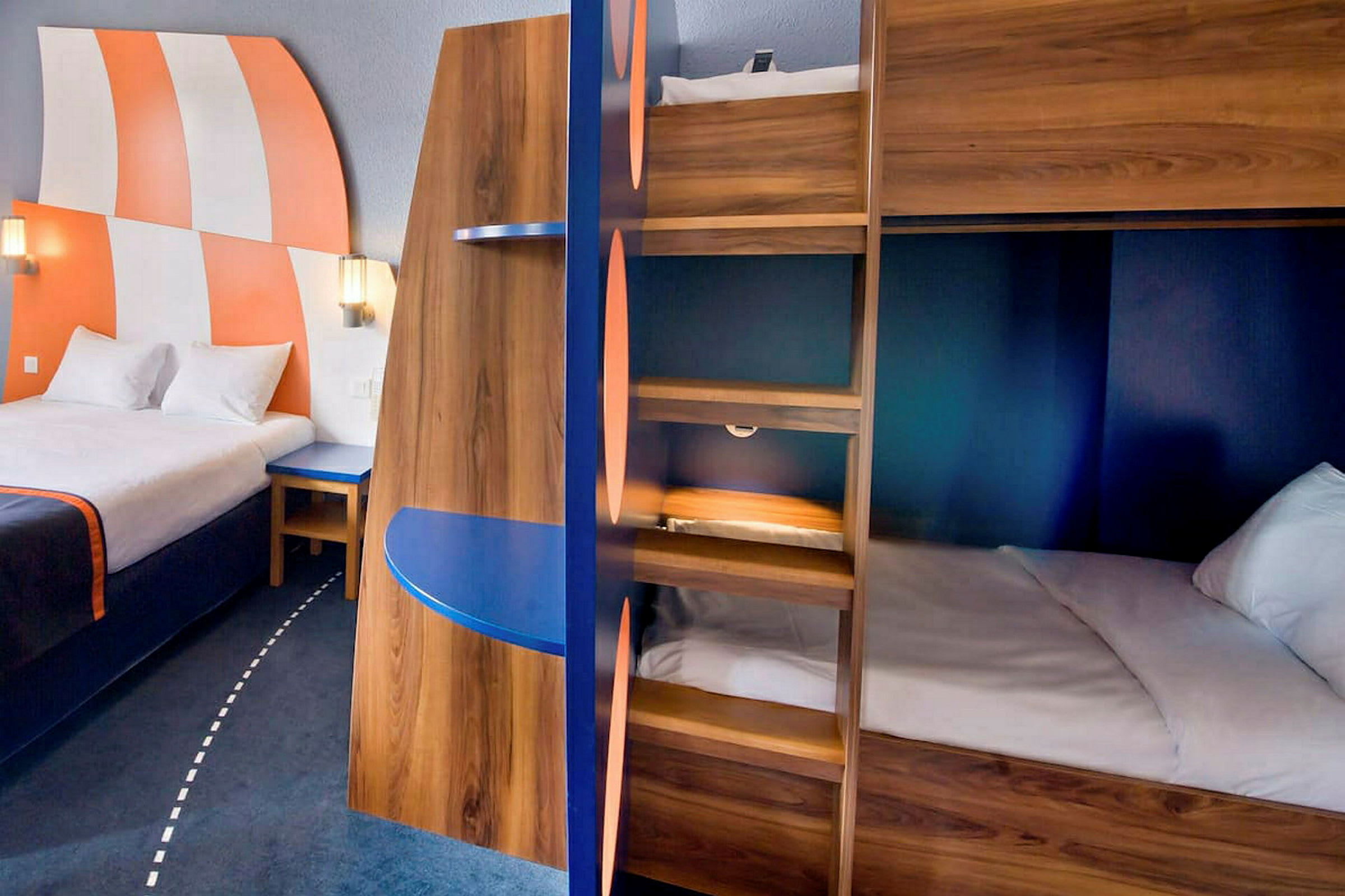 Hotellihuoneen sisustus, jossa on iso sänky, kerrossängyt ja värikkäitä yksityiskohtia. (Tekoälyn luoma teksti)