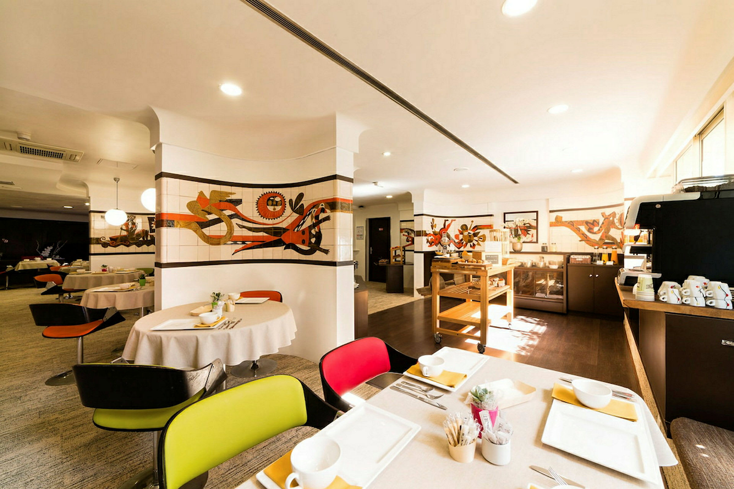 Ravintola, jossa on katettuja pöytiä, seinillä taidetta ja tarjoilupiste. Valaistus on lämmin ja kutsuva. (Tekoälyn luoma teksti)