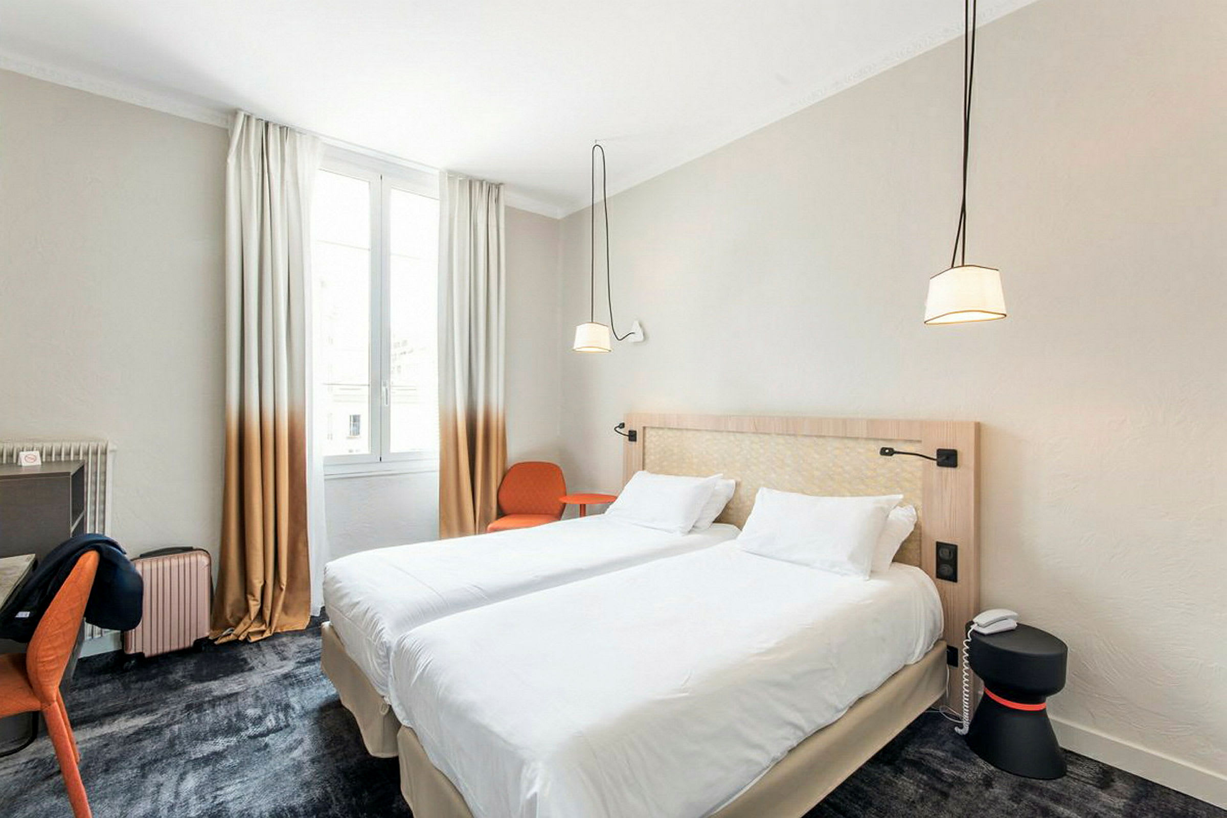 Hotellihuone, jossa on kaksi yhdistettyä erillissänkyä, kirjoituspöytä, tuoli ja ikkuna valon tuomiseksi. (Tekoälyn luoma teksti)