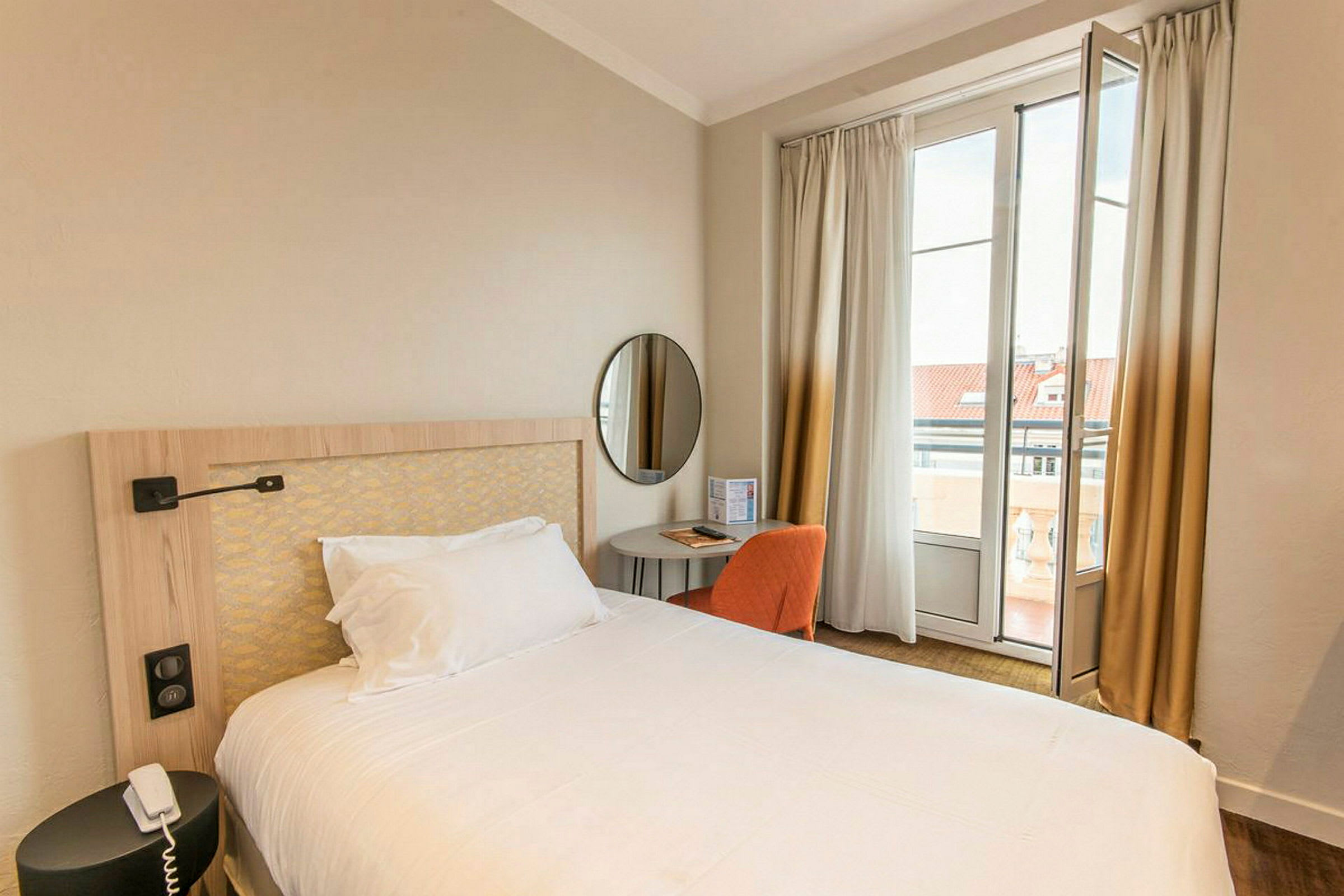 Hotellihuone, jossa on pedattu sänky, pieni pöytä ja tuoli ikkunan edessä verhon kanssa. (Tekoälyn luoma teksti)