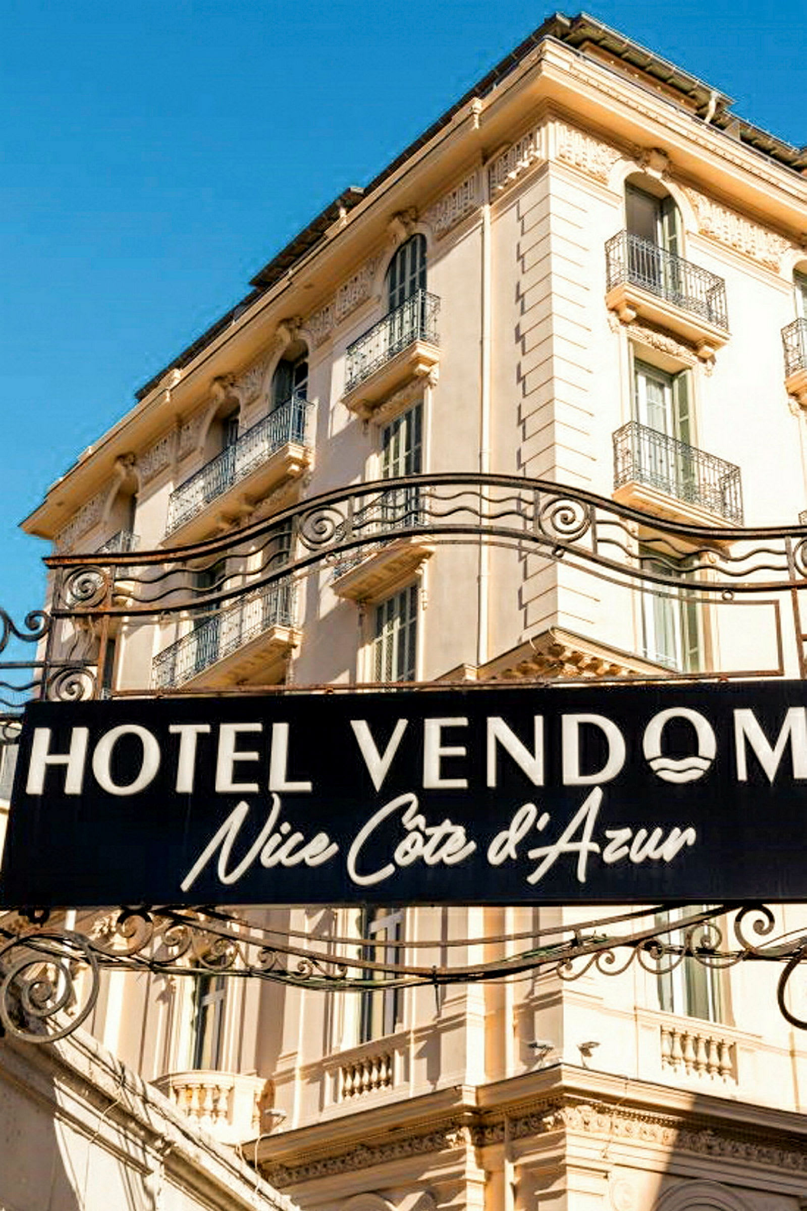 Kyltissä lukee Hotel Vendome Nice Côte d’Azur vaalean rakennuksen edessä. (Tekoälyn luoma teksti)
