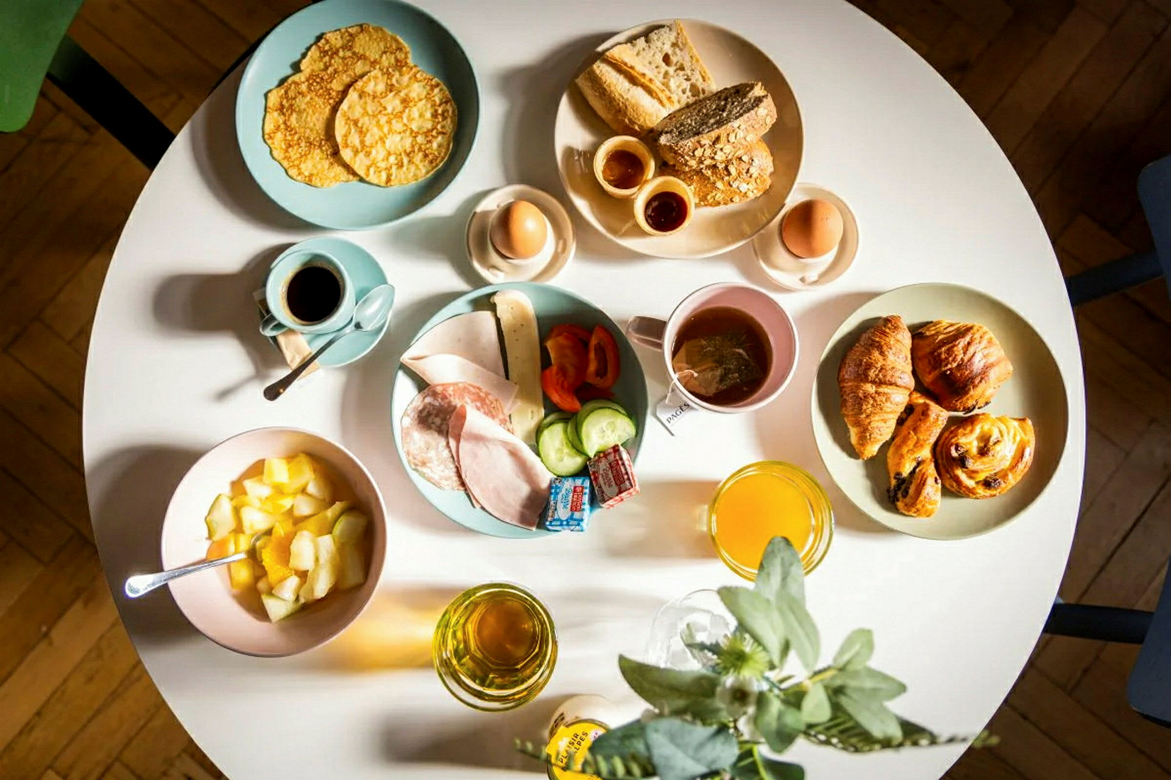 Aamiaislautasten, jossa leipää, leivonnaisia, munia, hedelmiä, leikkeleitä ja juomia. (Tekoälyn luoma teksti)