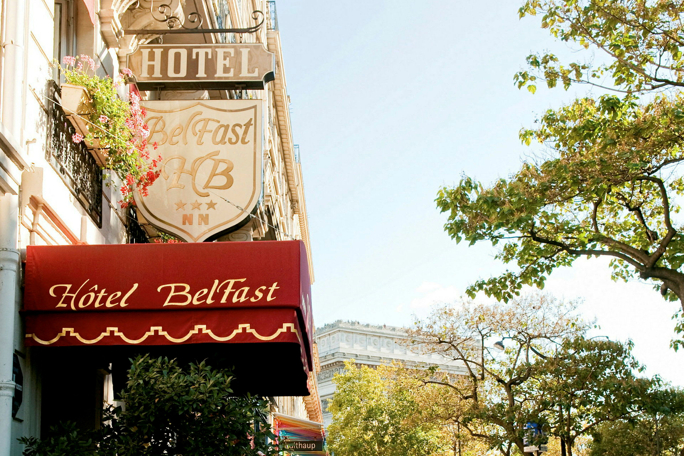Hotel Belfastin julkisivu kyltteineen ja läheisiä puita. (Tekoälyn luoma teksti)