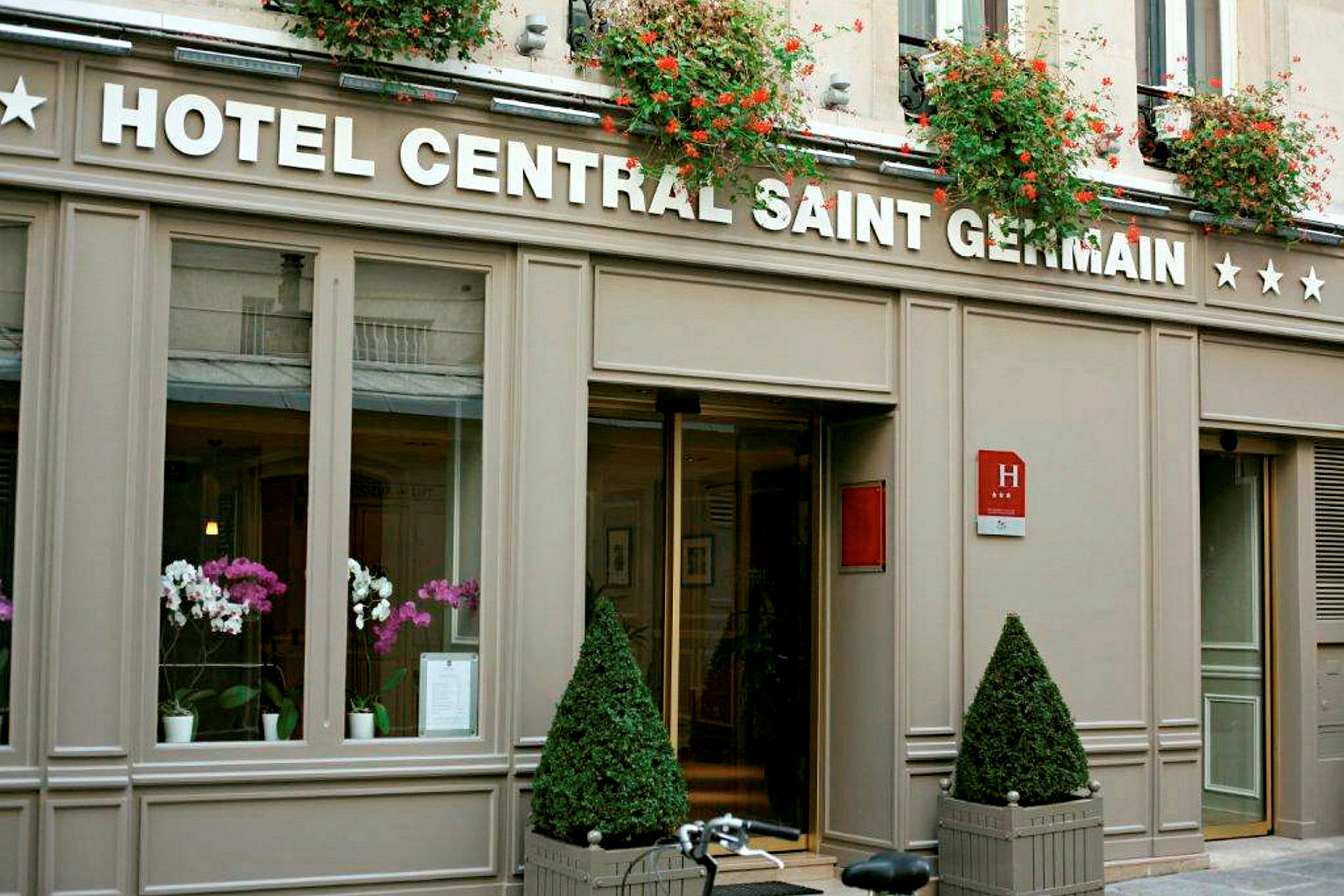 Kuva Hotel Central Saint Germainin hotellin sisäänkäynnistä, jossa on kukkakoristeita ja kyltti näkyvillä. (Tekoälyn luoma teksti)