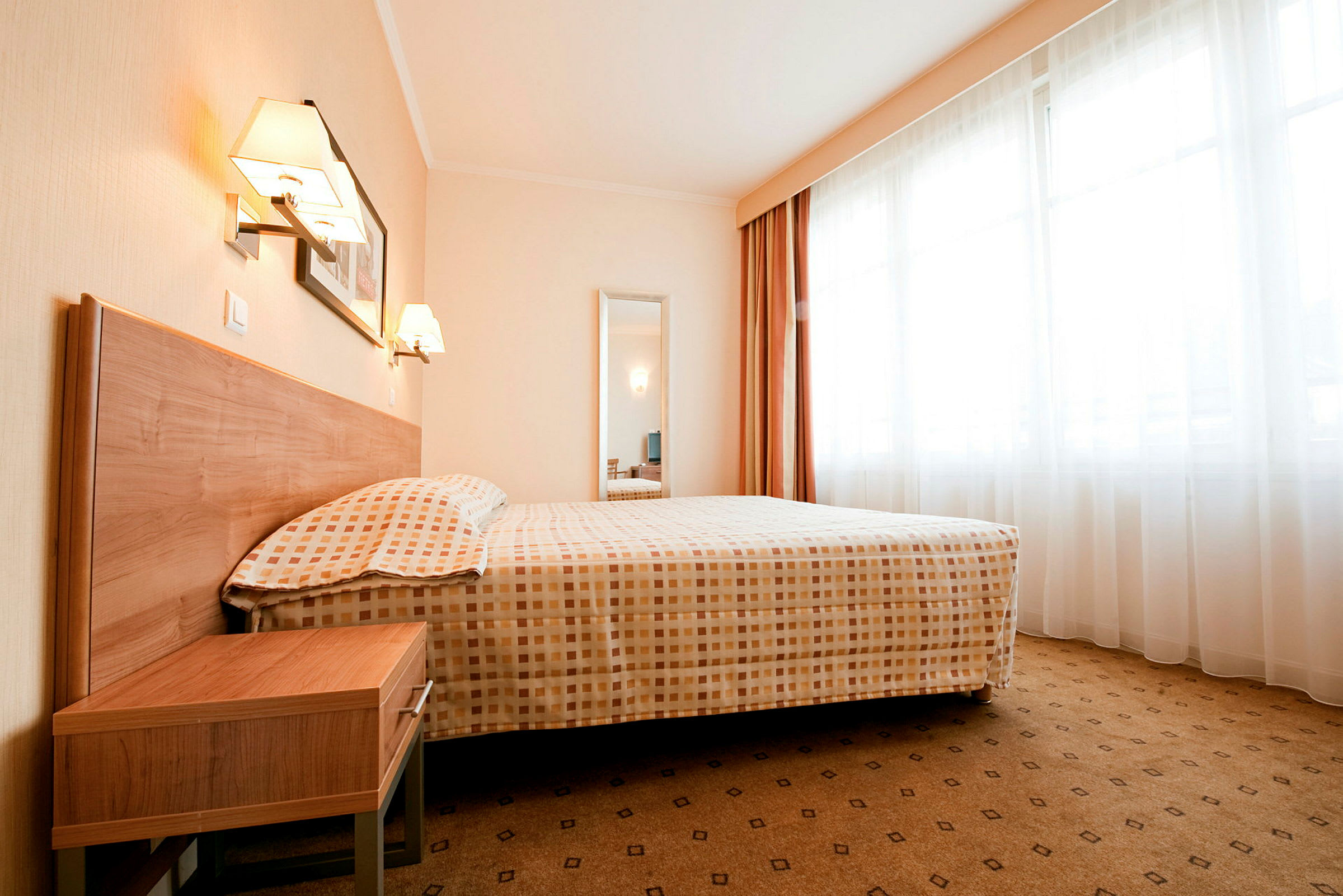 Hotellihuone, jossa on suuri sänky, yöpöytä ja ikkunat verhoilla. (Tekoälyn luoma teksti)
