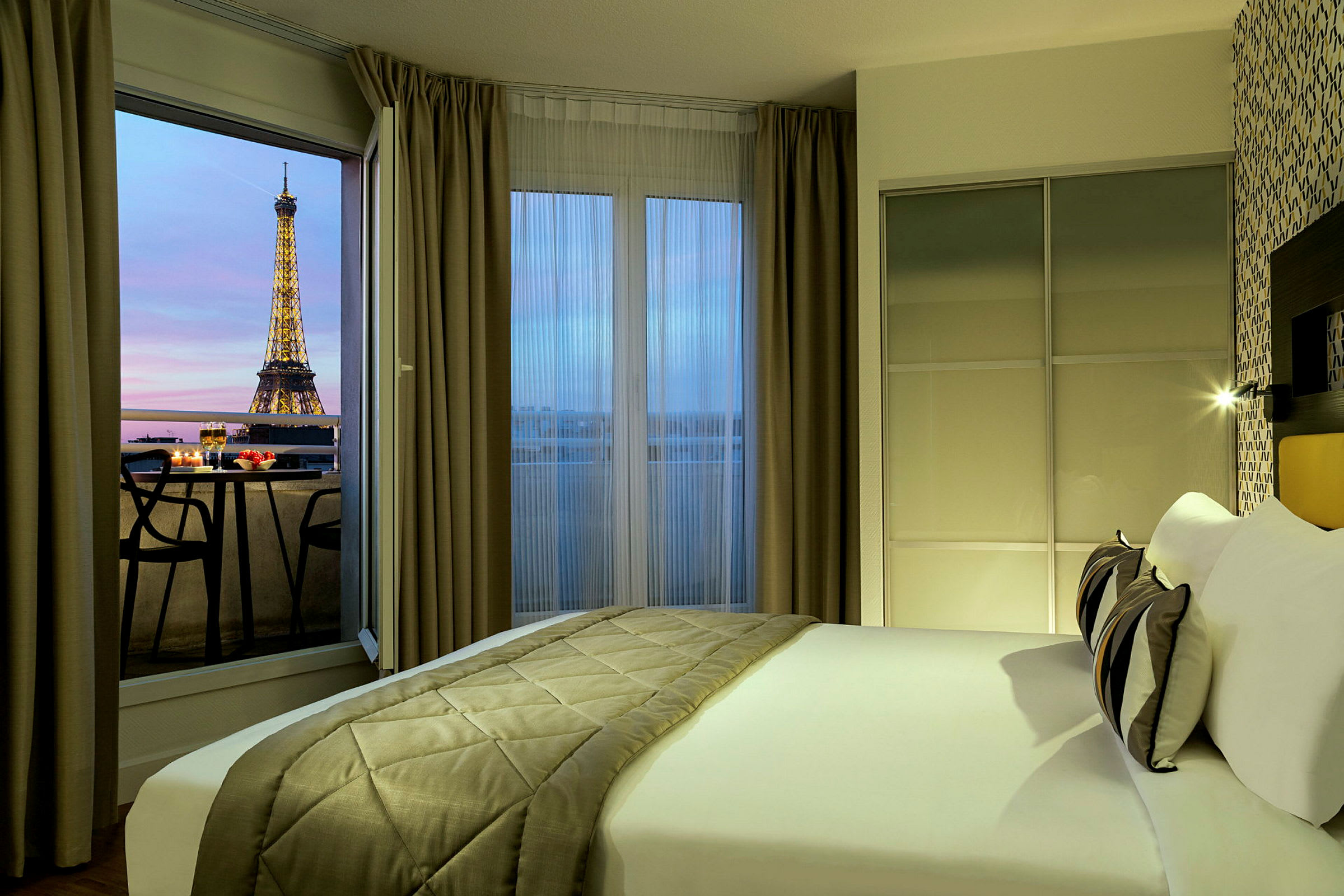 Hotellihuone, jossa on sijattu sänky, avoin parvekkeen ovi ja näkymä Eiffel-tornille. (Tekoälyn luoma teksti)