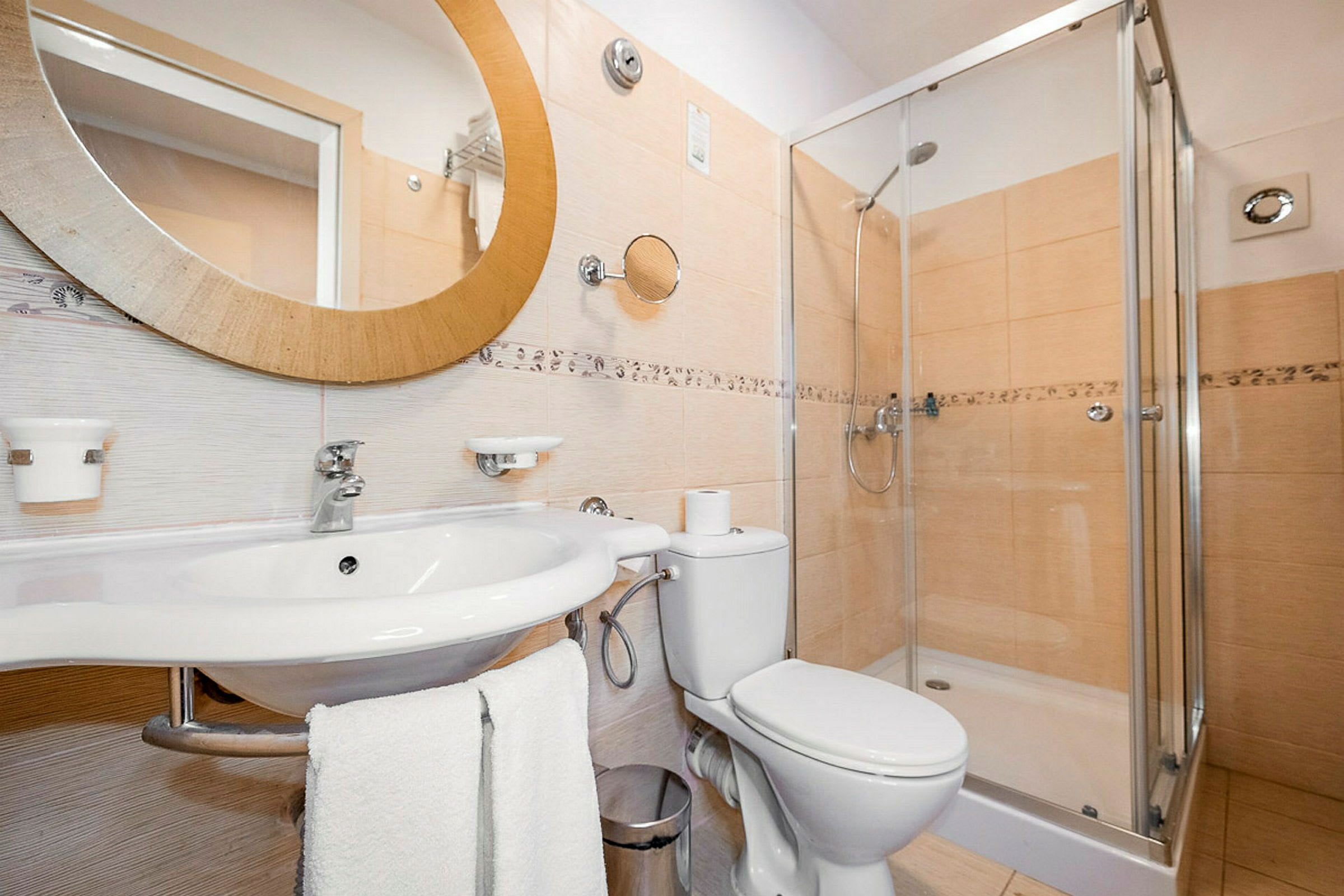Kylpyhuone, jossa valkoinen pesuallas, pyöreä peili, wc-istuin ja suihkukaappi. (Tekoälyn luoma teksti)