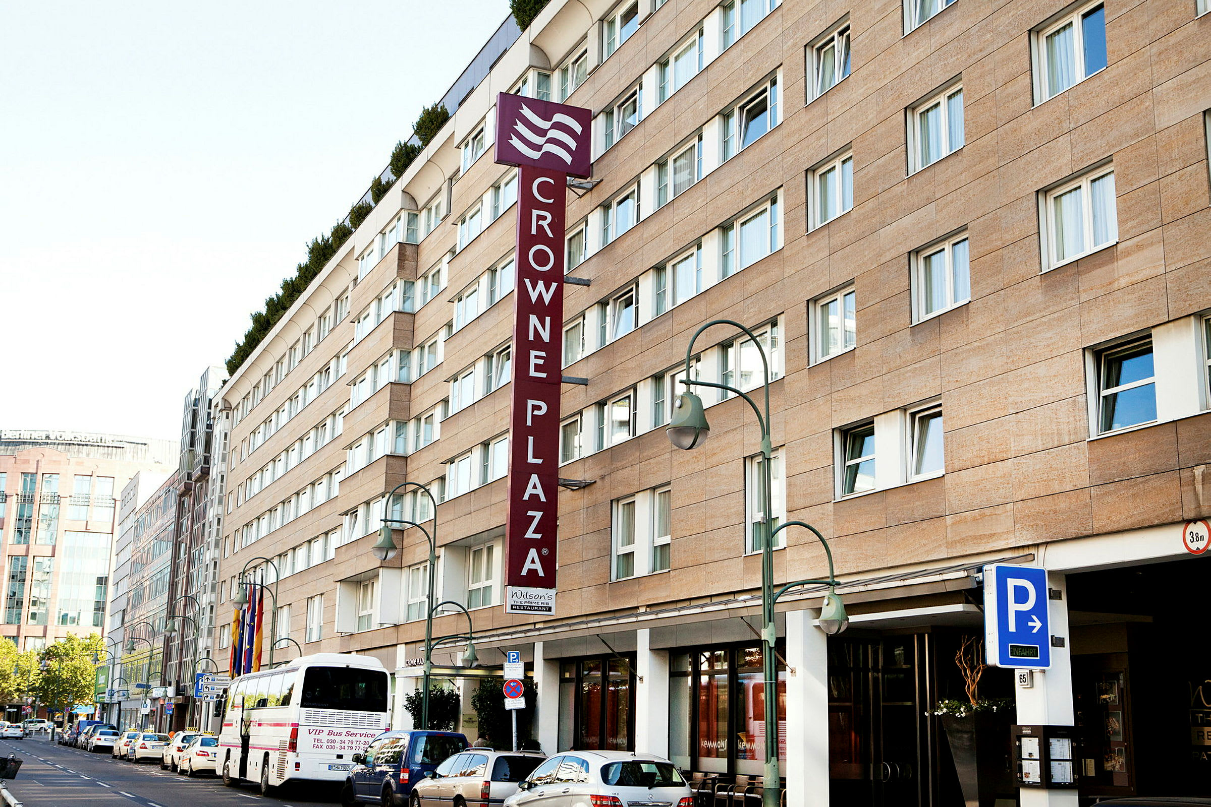 Crowne Plaza -hotellirakennus, jossa pysäköintimerkki ja bussi edessä. (Tekoälyn luoma teksti)