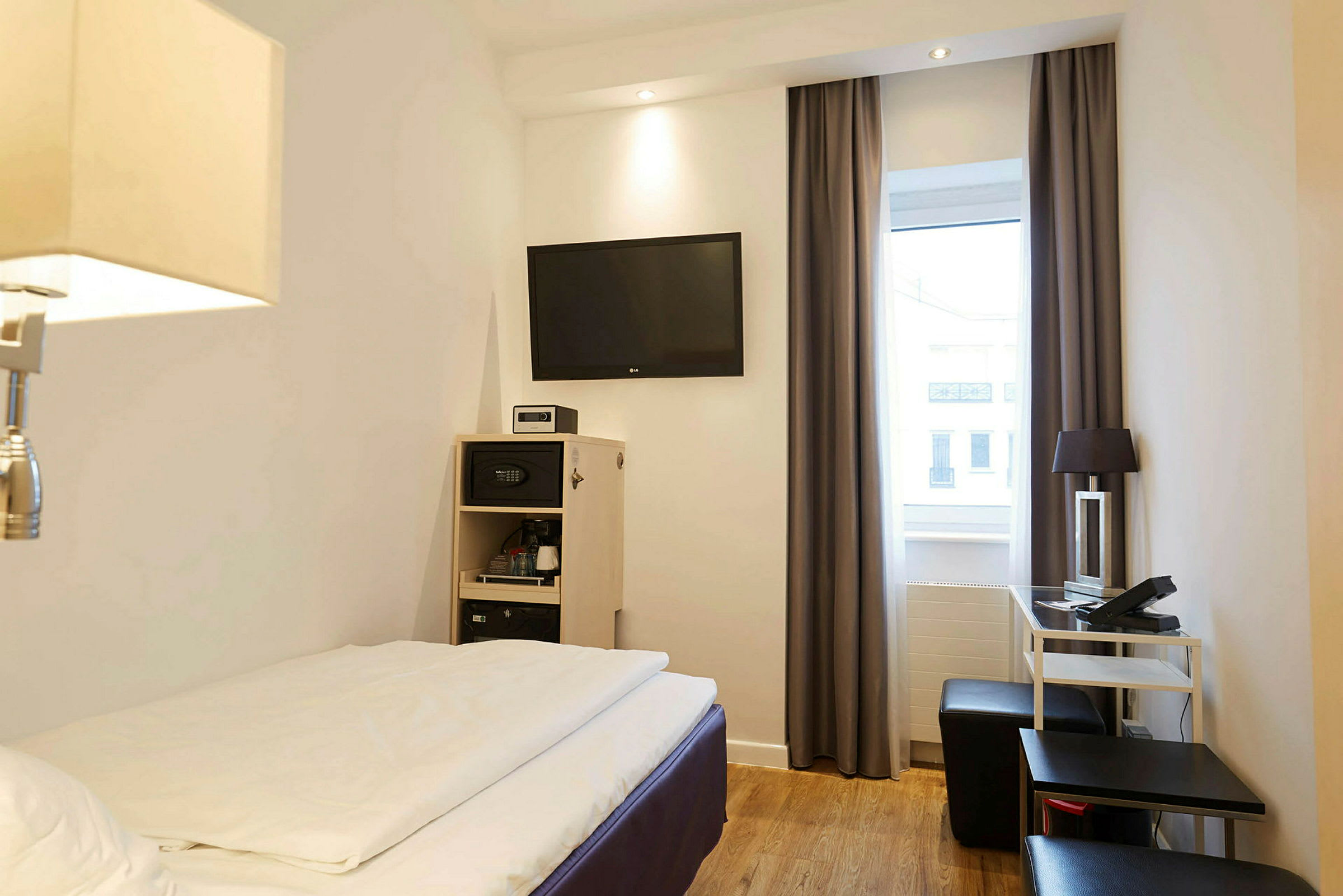 Hotellihuone, jossa on sänky, seinällä tv sekä huonekaluja kuten kirjoituspöytä ja tuoli. (Tekoälyn luoma teksti)